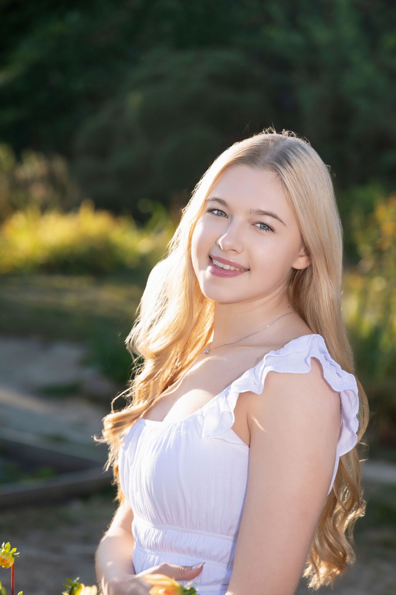 Summer portrait in white dress with sunlit garden backdrop.