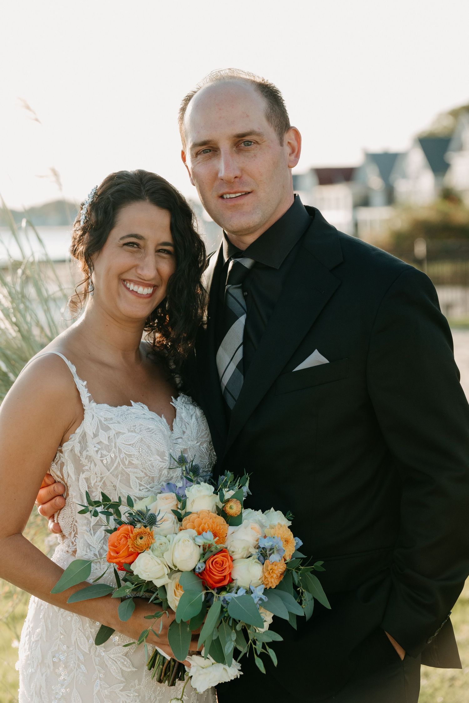 Couple in formal wedding attire pose with colorful bouquet outdoors.