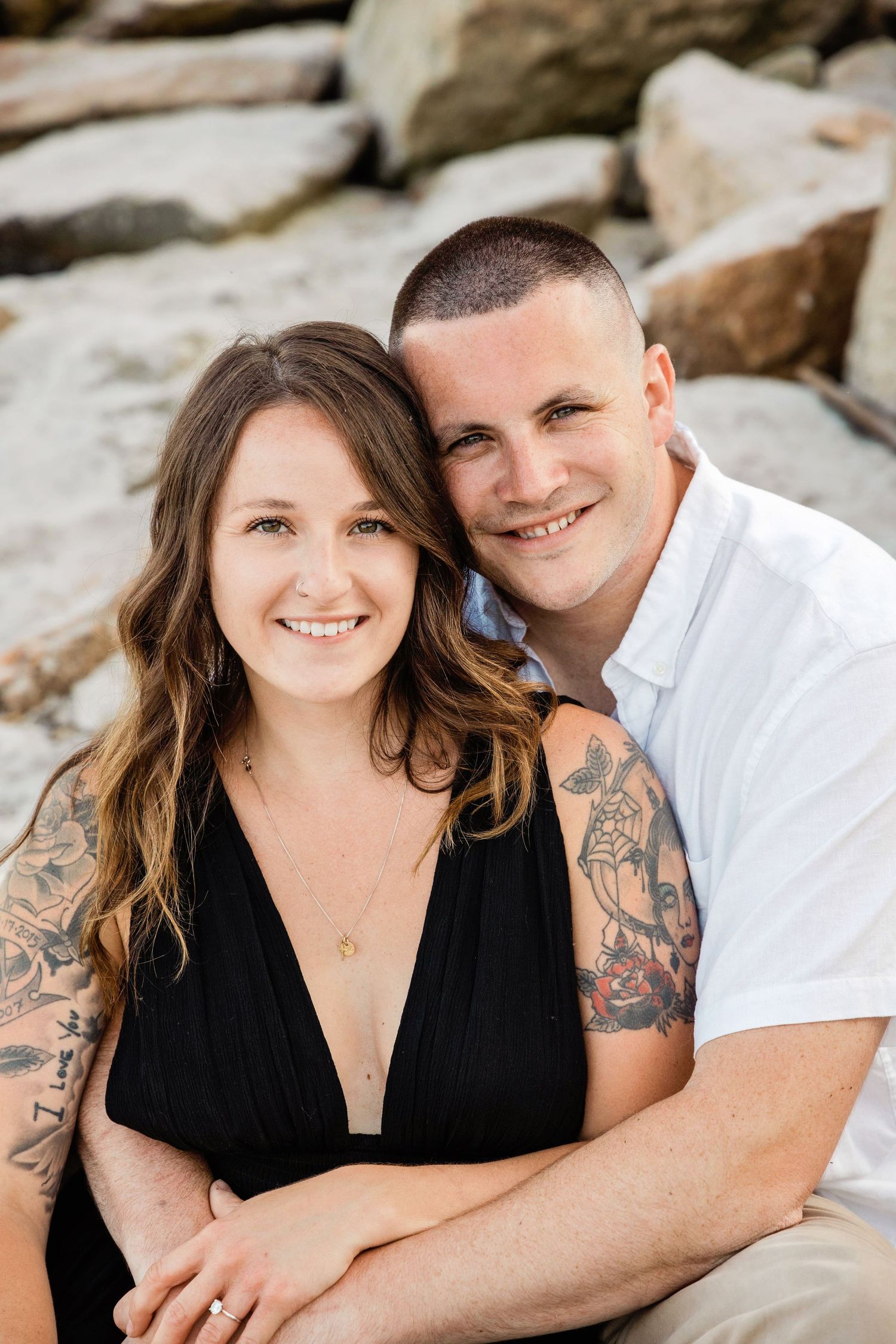 A couple shares intimate moments while posing for romantic photos on a rocky beach setting.