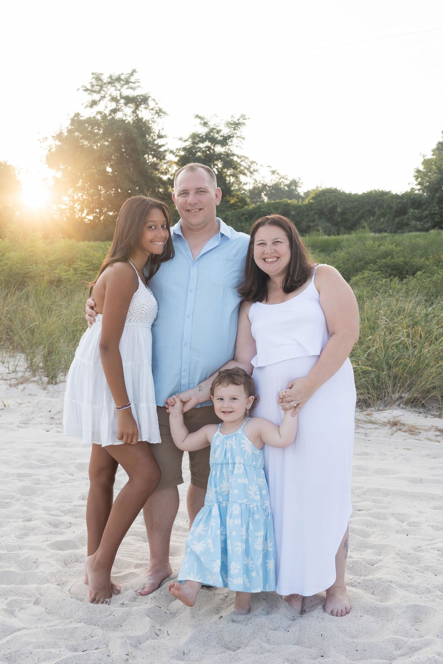 Family poses together on sandy beach during golden hour sunset photo session.