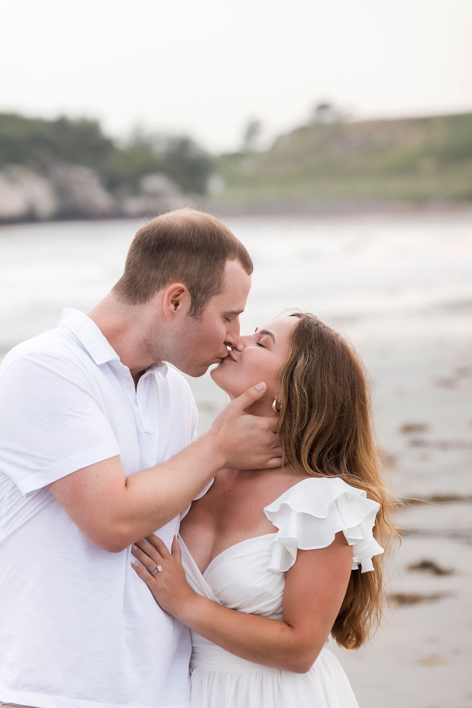 A romantic couple in white outfits sharing intimate kisses on a sandy beach at sunset.