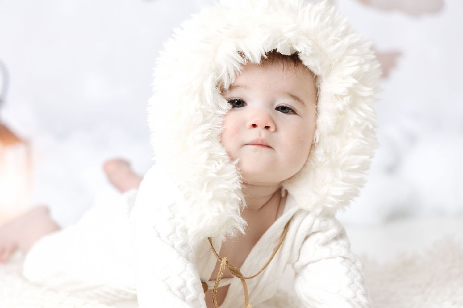 A young child in a white fur-trimmed hood looks up dreamily against a bright white background.
