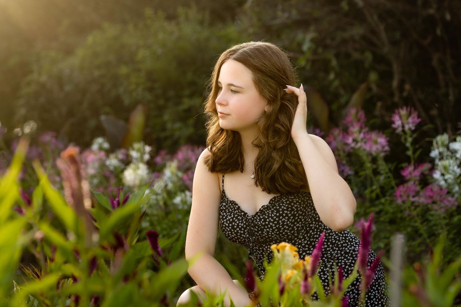 A person in a polka dot dress stands in a lush garden with blooming flowers at golden hour.