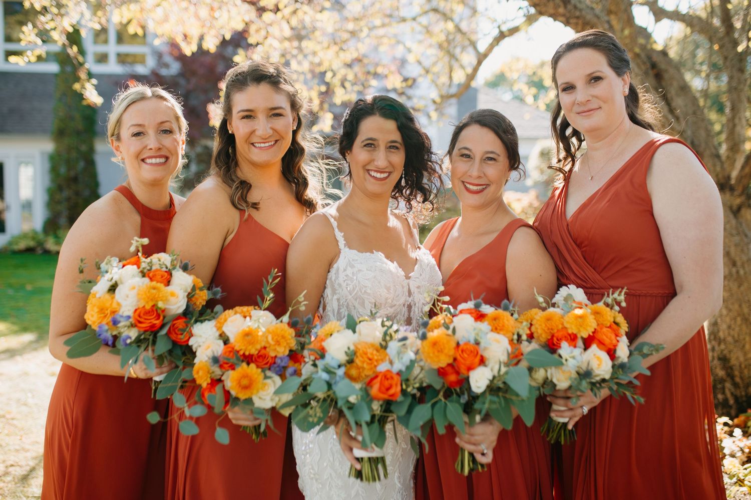 Bridal party in rust-colored dresses holding vibrant orange and white bouquets.