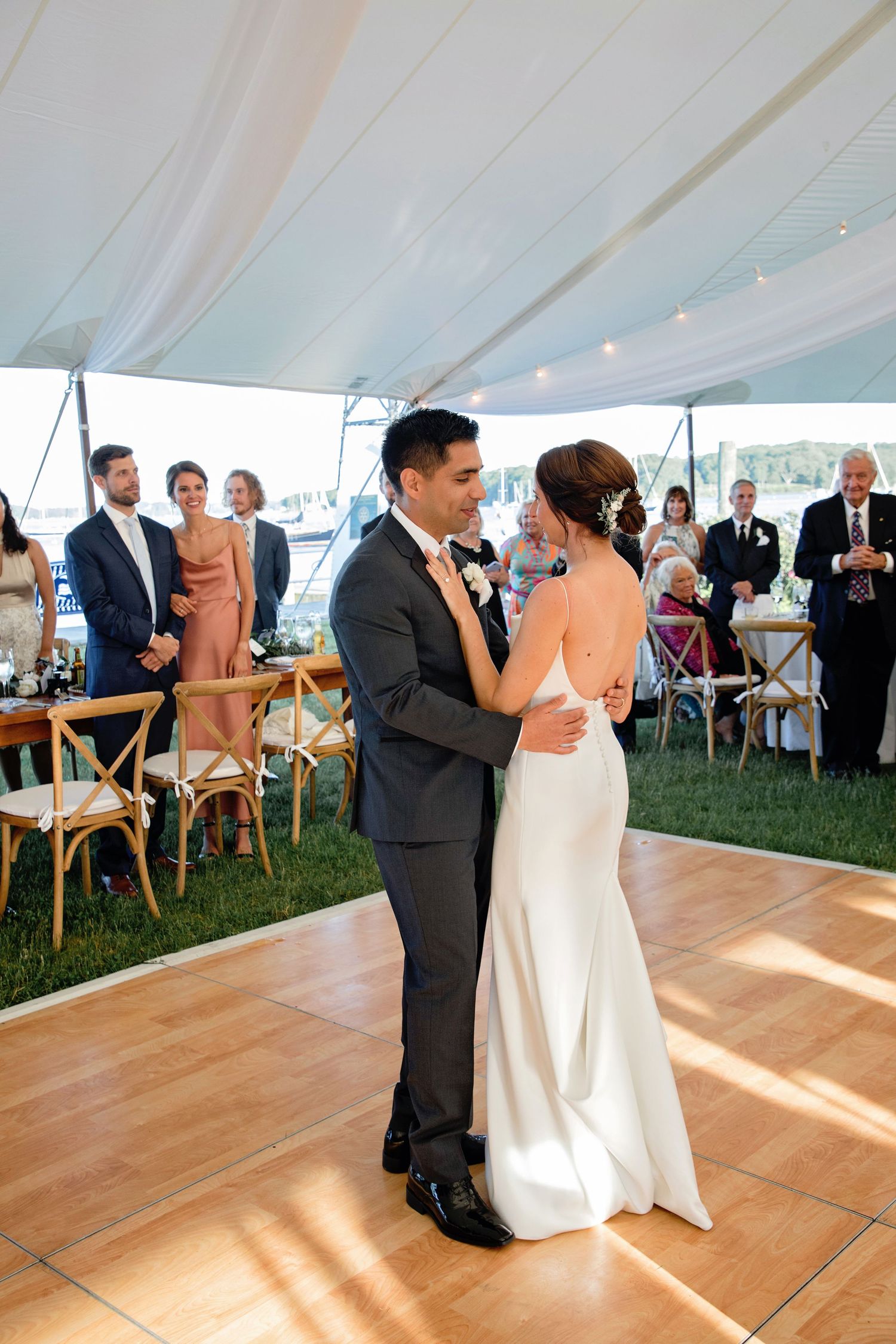 A couple shares their first dance together on a wooden floor under an elegant white tent at a wedding reception.
