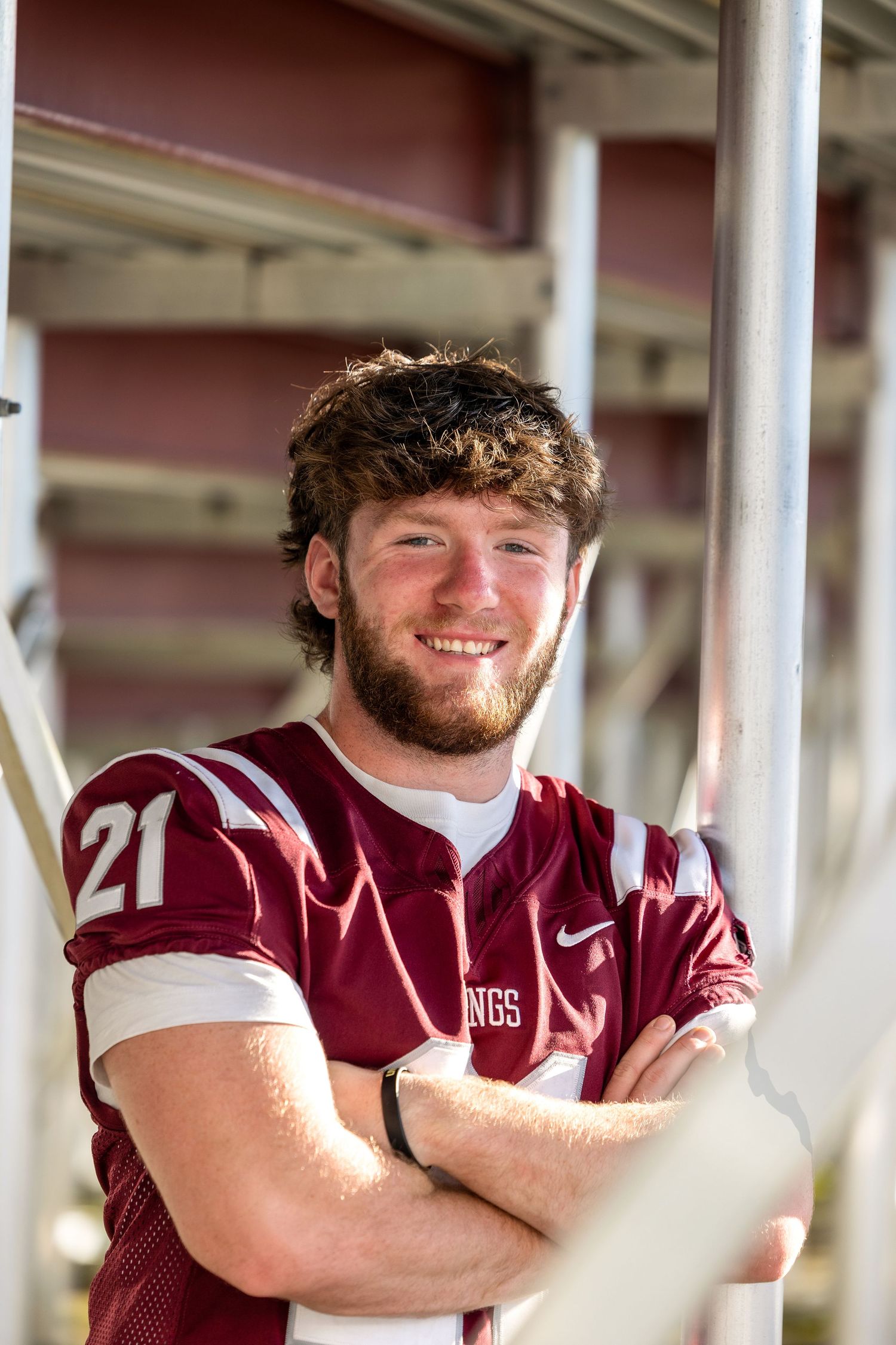 Athlete in maroon uniform poses confidently under stadium bleachers.