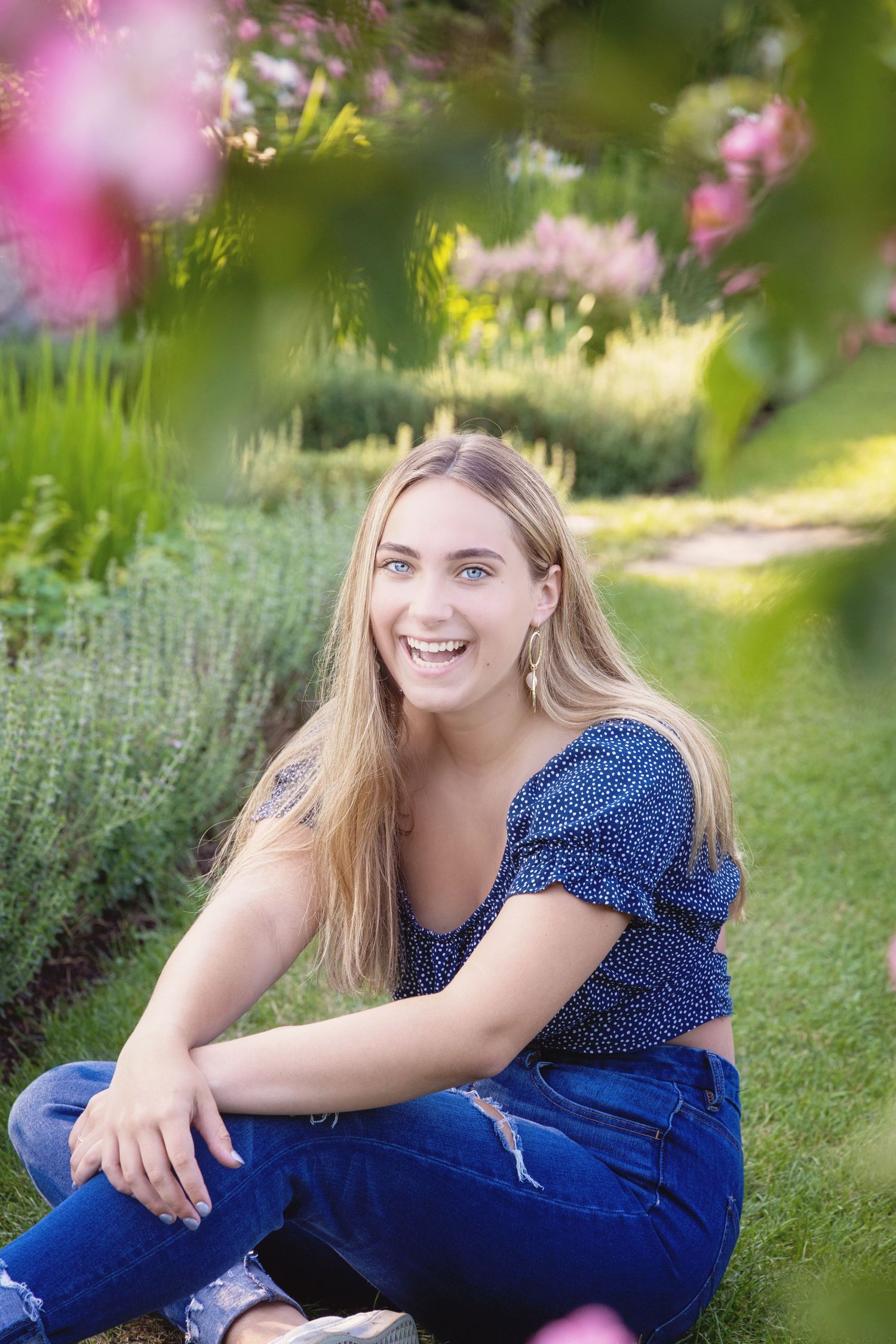 A person in a blue polka dot top and jeans relaxes on green grass in a sunny garden setting.