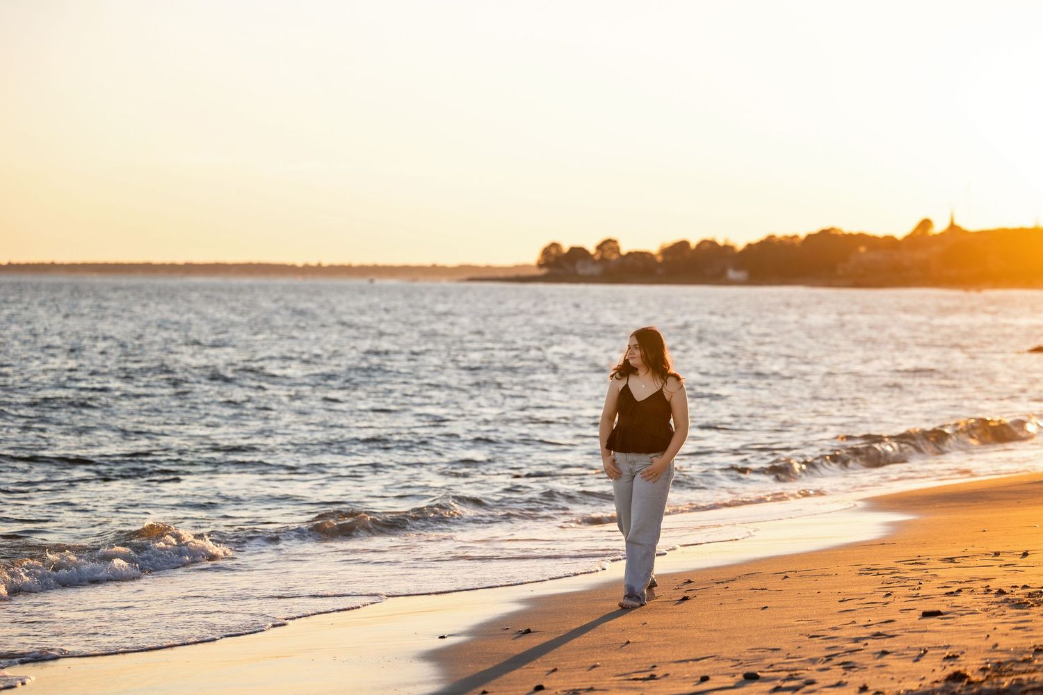 Silhouetted figure walking along beach shoreline during golden sunset.