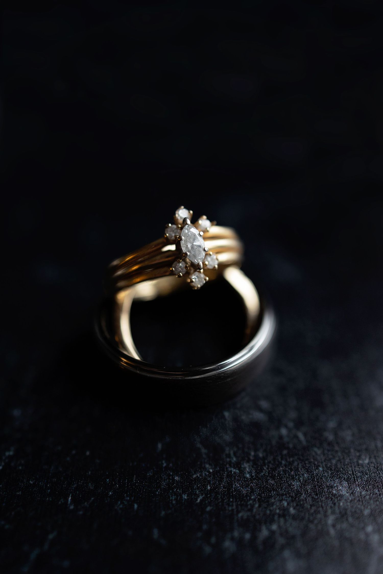 Wedding rings photographed in dramatic lighting on dark textured surface.