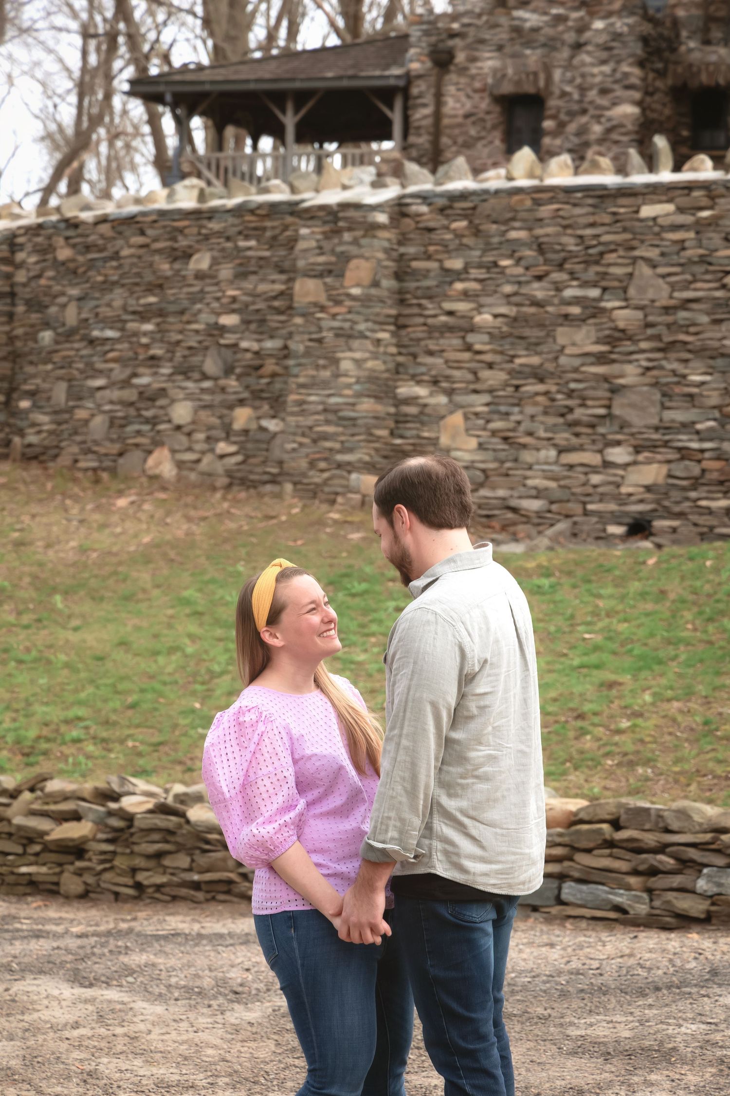 A couple shares a romantic moment in front of a rustic stone wall on a spring day.
