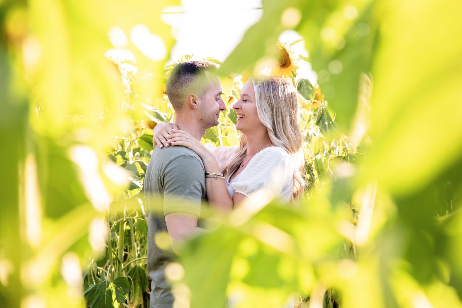 Romantic couple embracing in a sunlit field with bright yellow and green bokeh effect in the background.