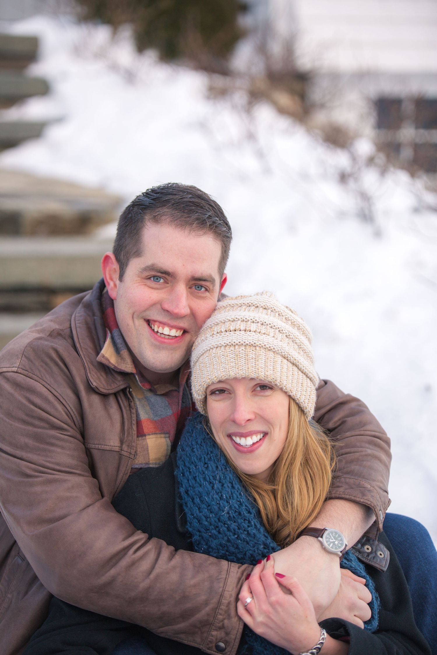 A couple embraces outdoors on a winter day with snow in the background.