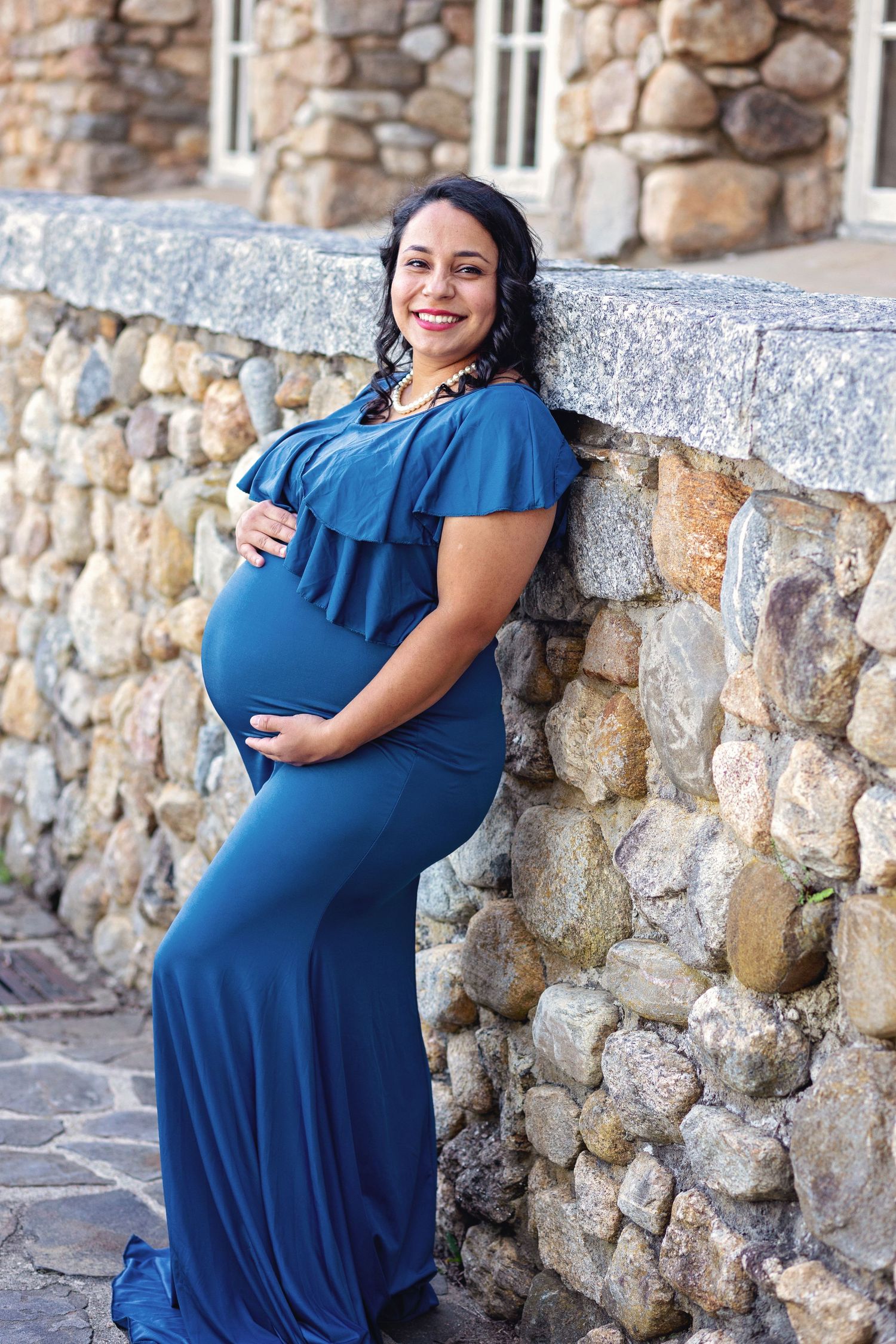 A series of maternity photos showing a woman in a blue dress posing against a rustic stone wall.