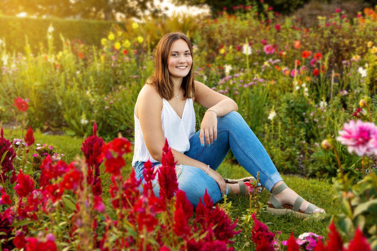 A person sits in a vibrant garden filled with blooming red and pink flowers during golden hour sunset.