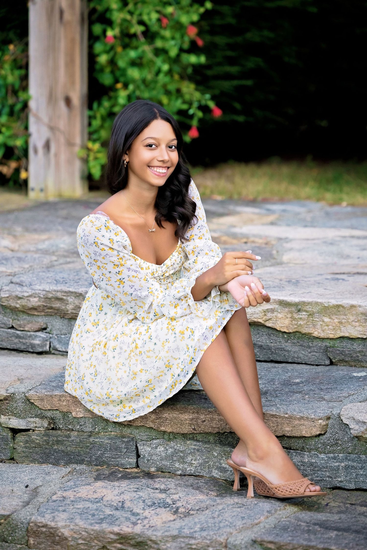 Someone in a floral dress sitting on stone steps in a summer garden setting.