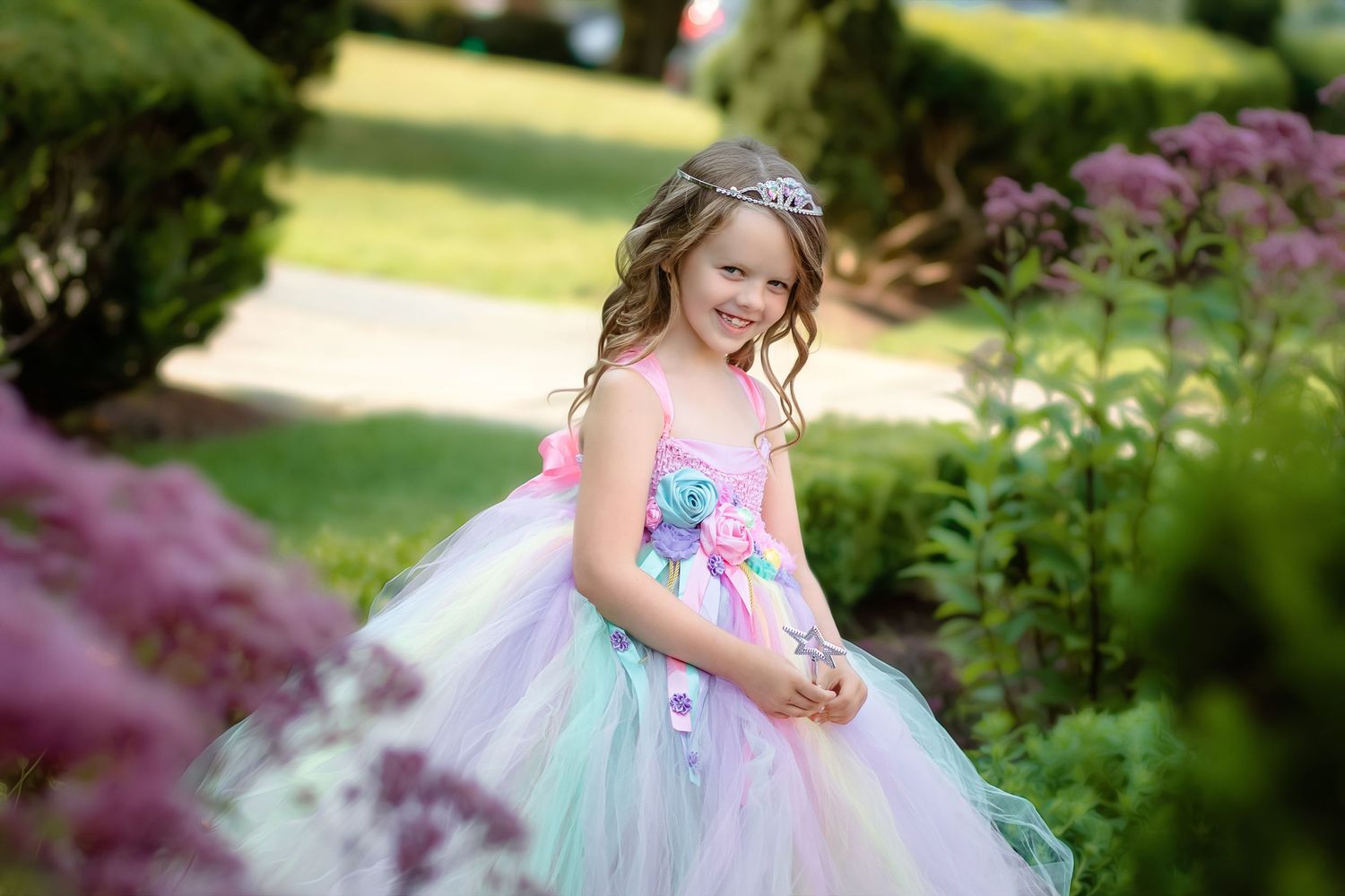 A child in a pastel tulle dress plays in a lush garden setting with blooming flowers and greenery.