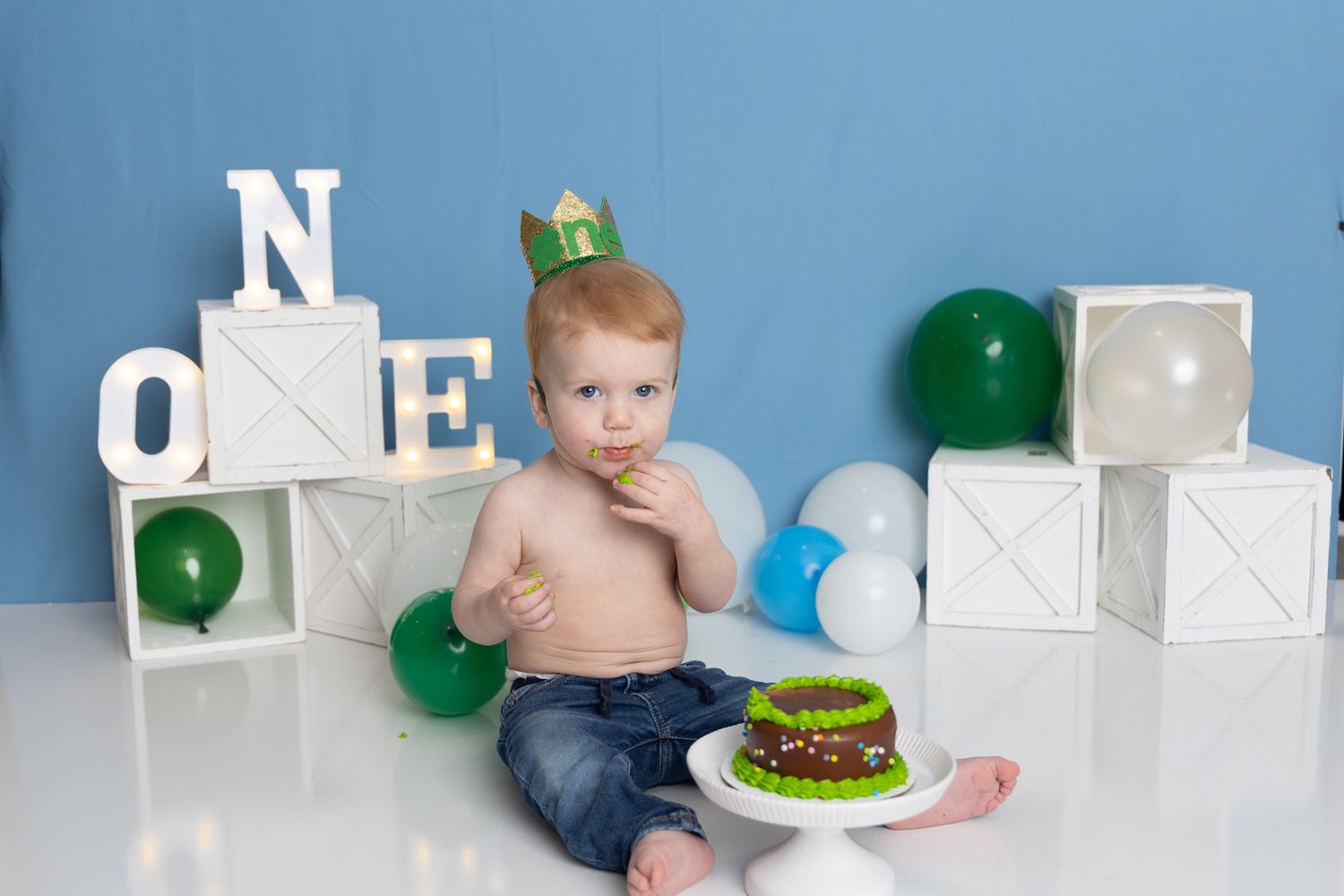 A baby sitting on a white backdrop with blocks and a green birthday cake in a progressive sequence of photos.