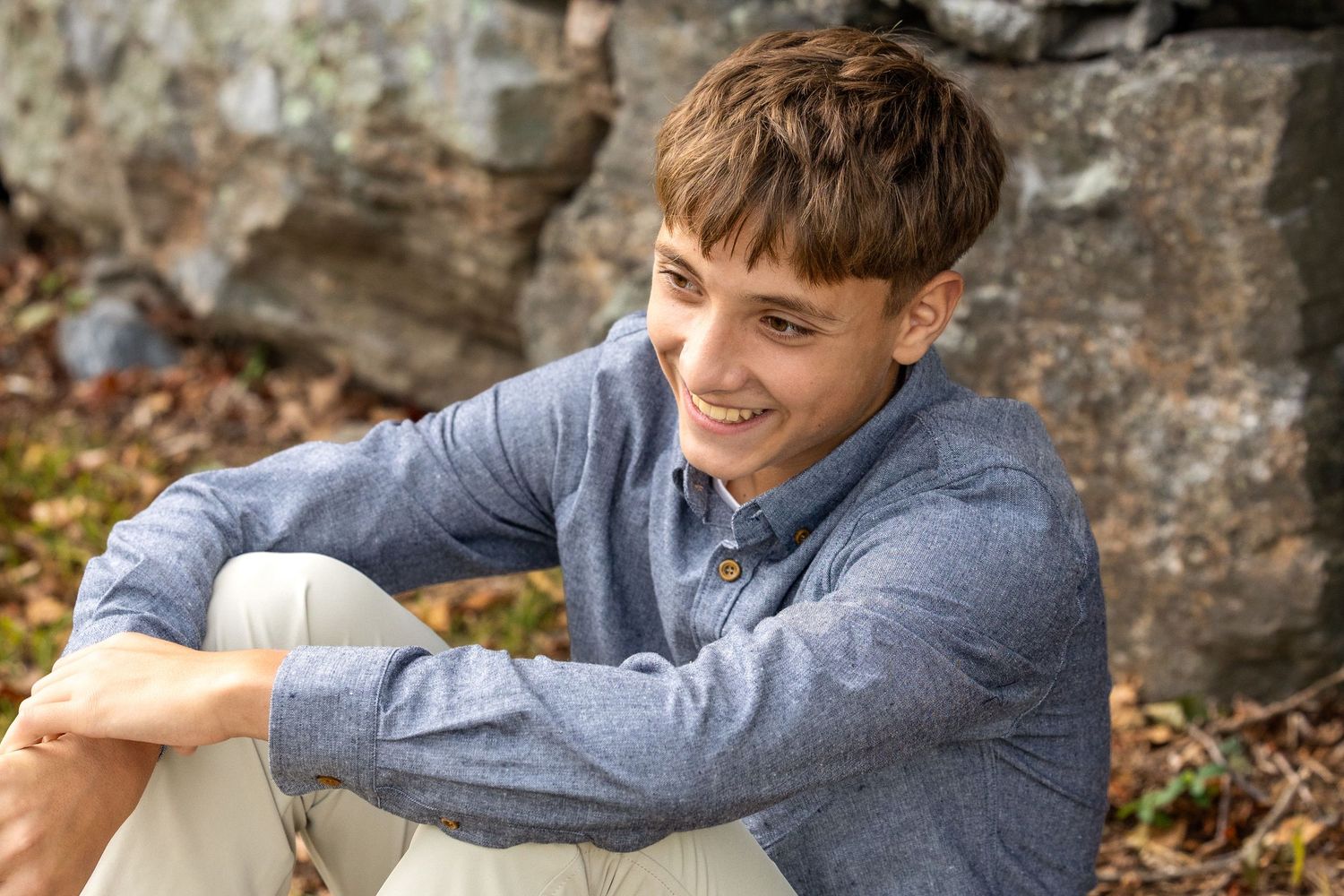 A person in a gray sweater sits on stone steps surrounded by autumn leaves and rustic stone walls.