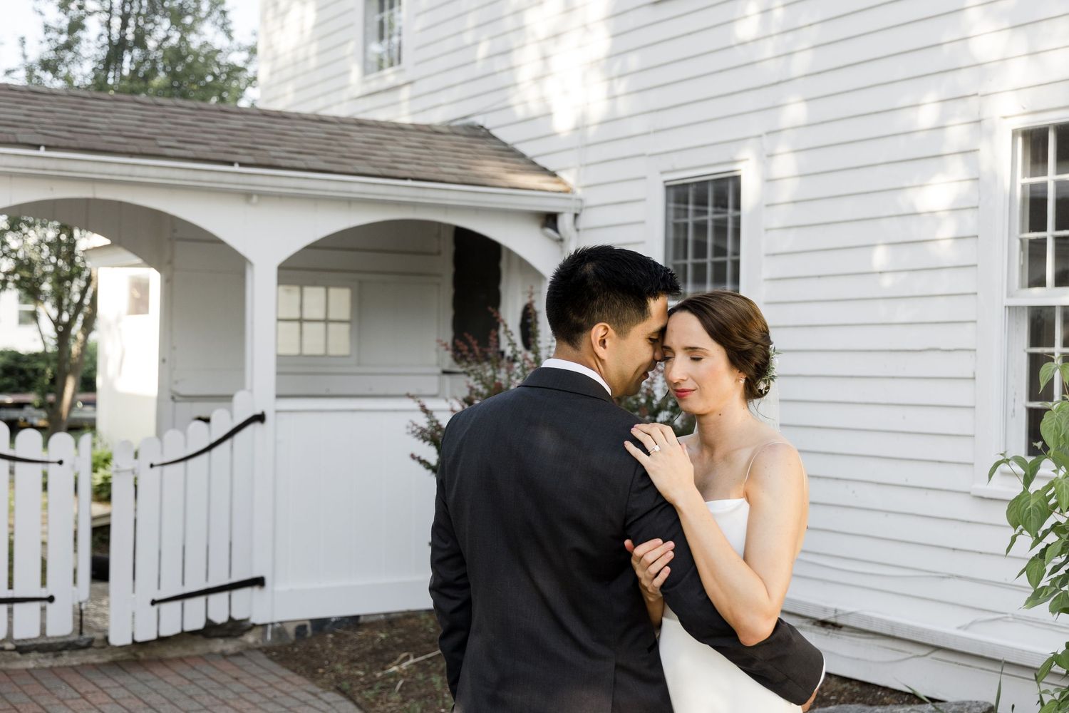 A romantic moment shared between a couple in formal attire outside a white church building.