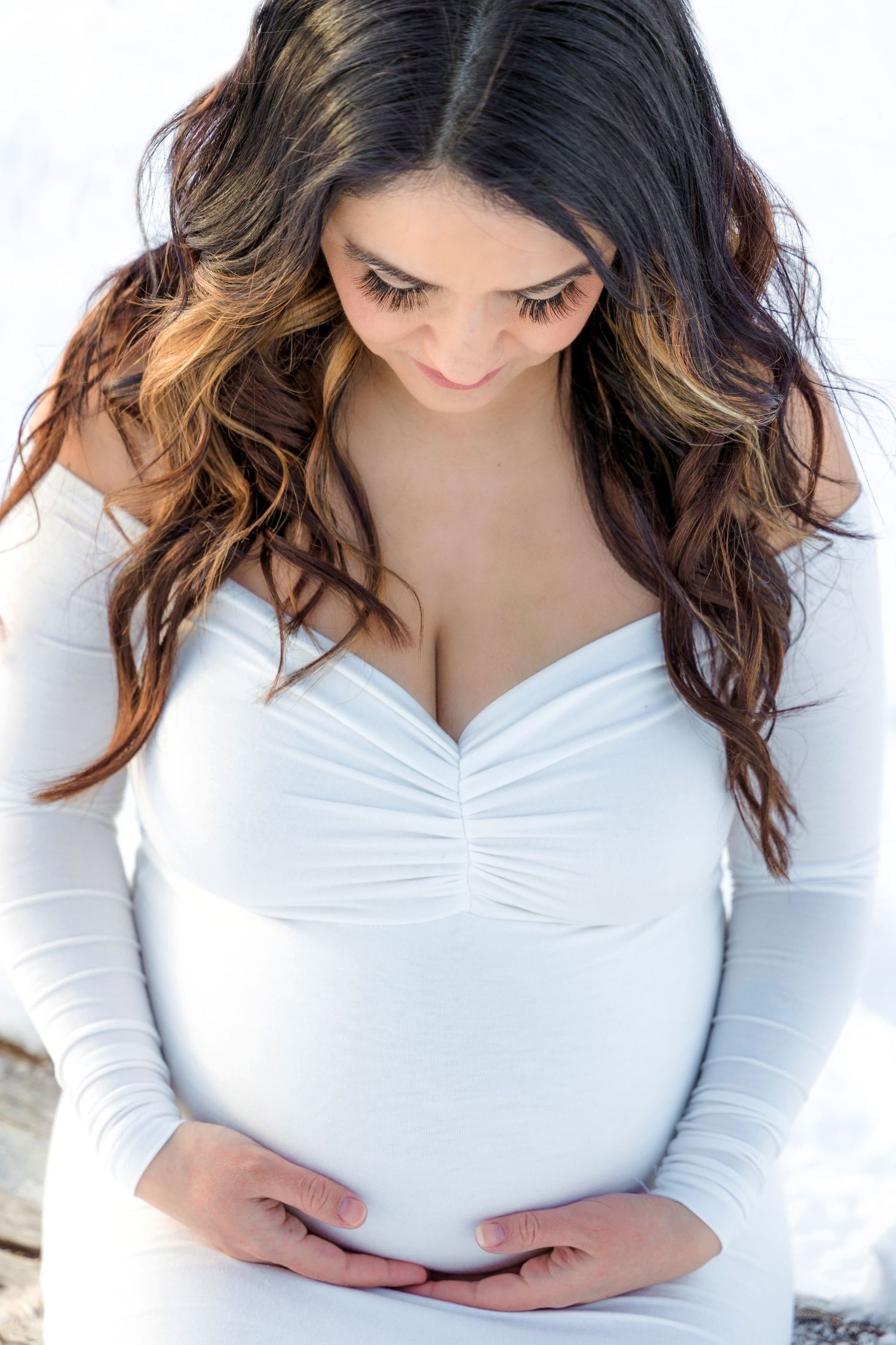 Woman in white long sleeve top with ombre brown hair poses against white background.