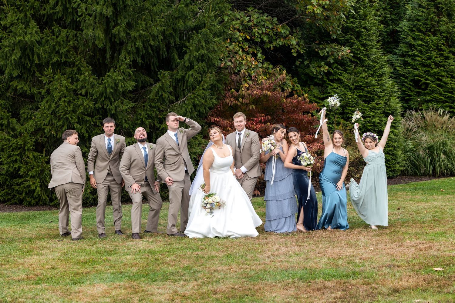 Wedding party celebrates outdoors with joyful poses against autumn foliage.