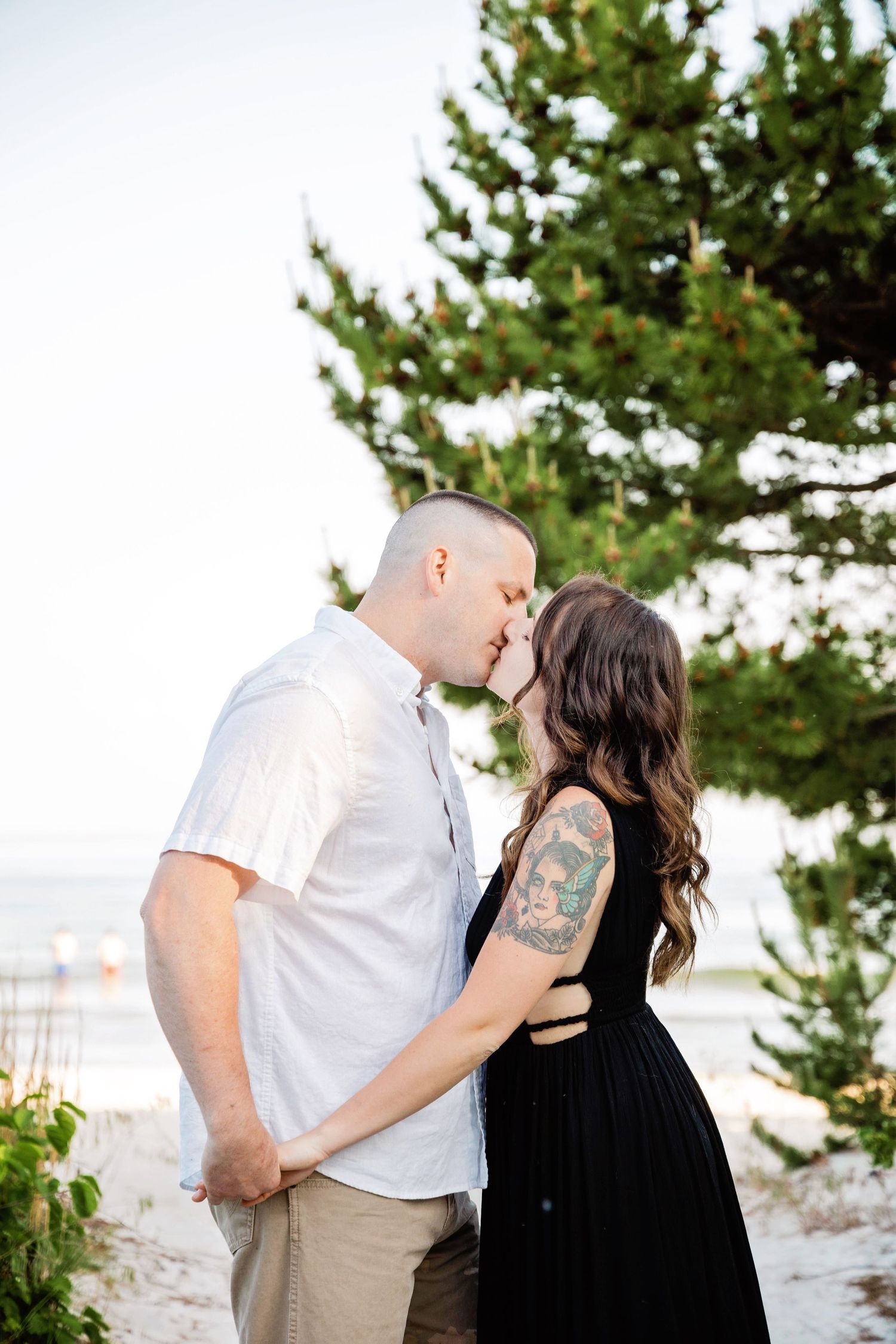 A romantic couple shares an intimate moment outdoors with evergreen trees in the background.