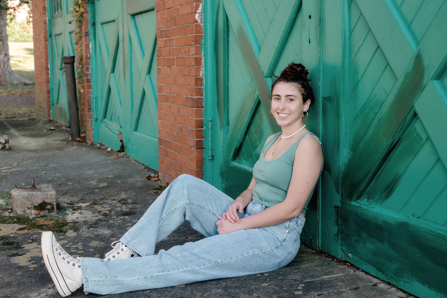 Someone in a light blue dress sits on stone steps against a turquoise wooden door in an outdoor setting.