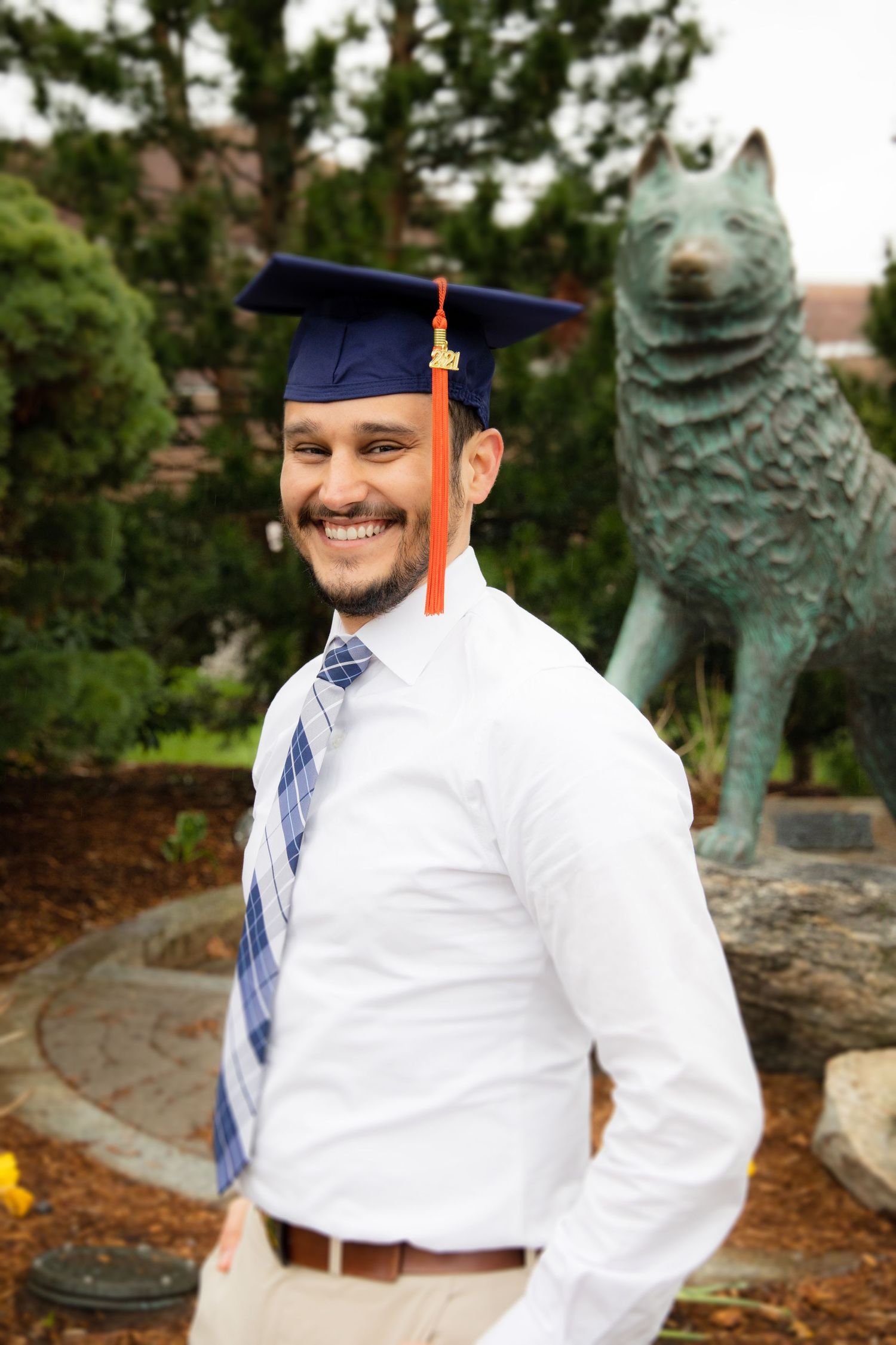 Graduate in cap and gown poses with university mascot statue during commencement celebration.
