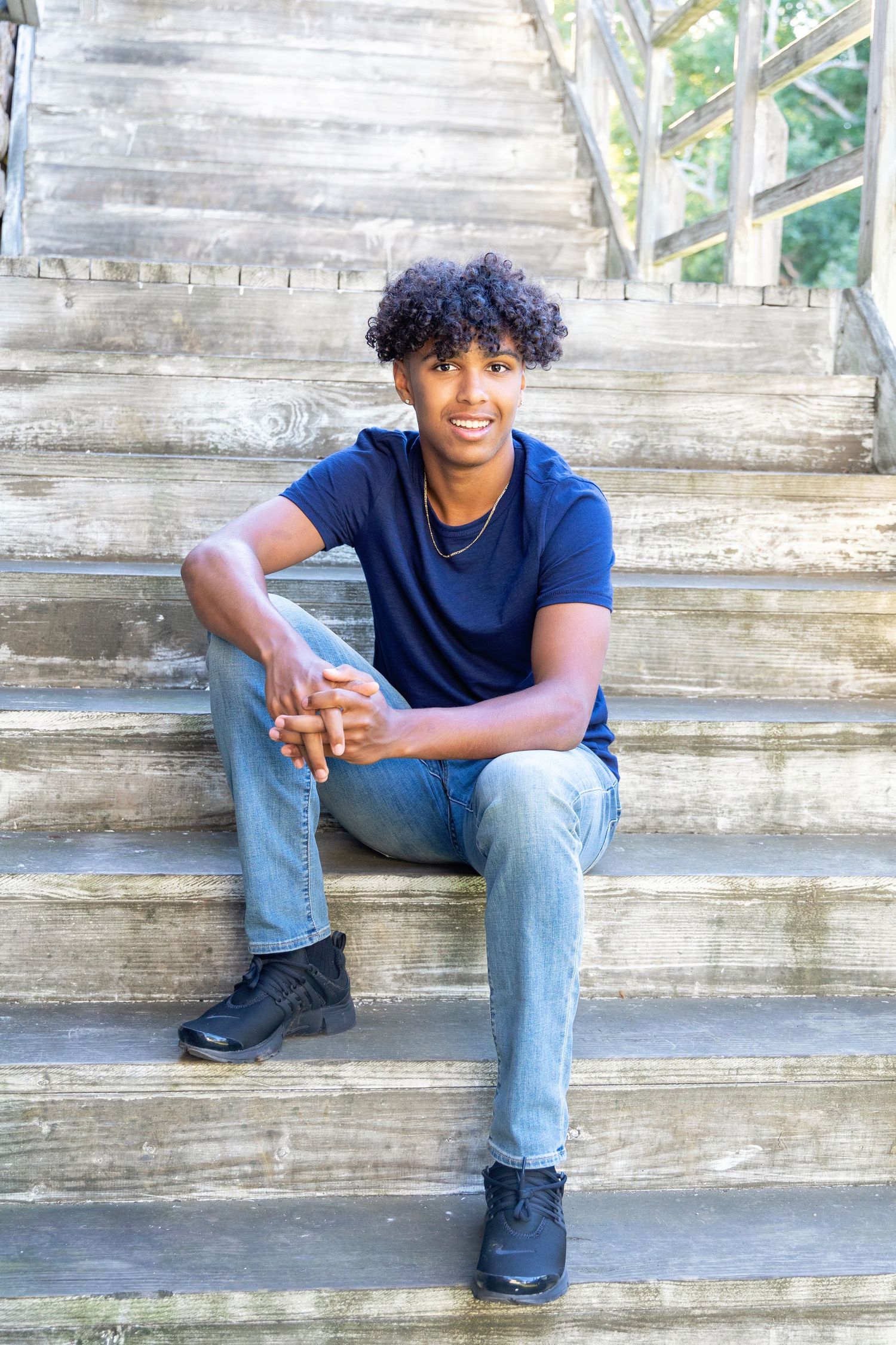 A person in a navy blue t-shirt and light jeans sits casually on concrete steps in an outdoor setting.