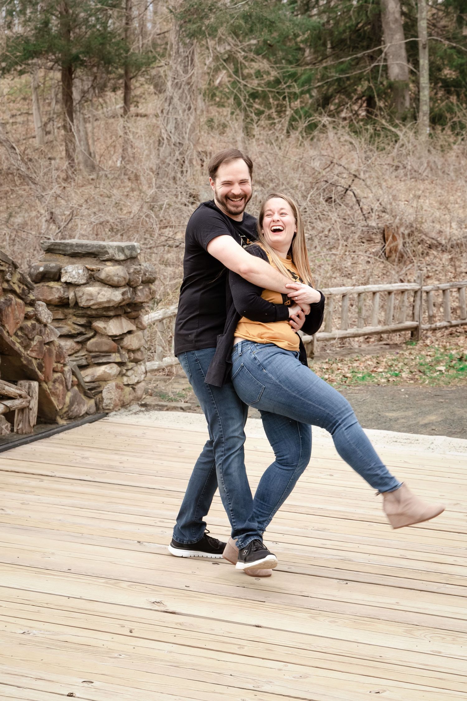 A playful sequence shows a couple laughing and falling over together on a wooden deck in a natural outdoor setting.