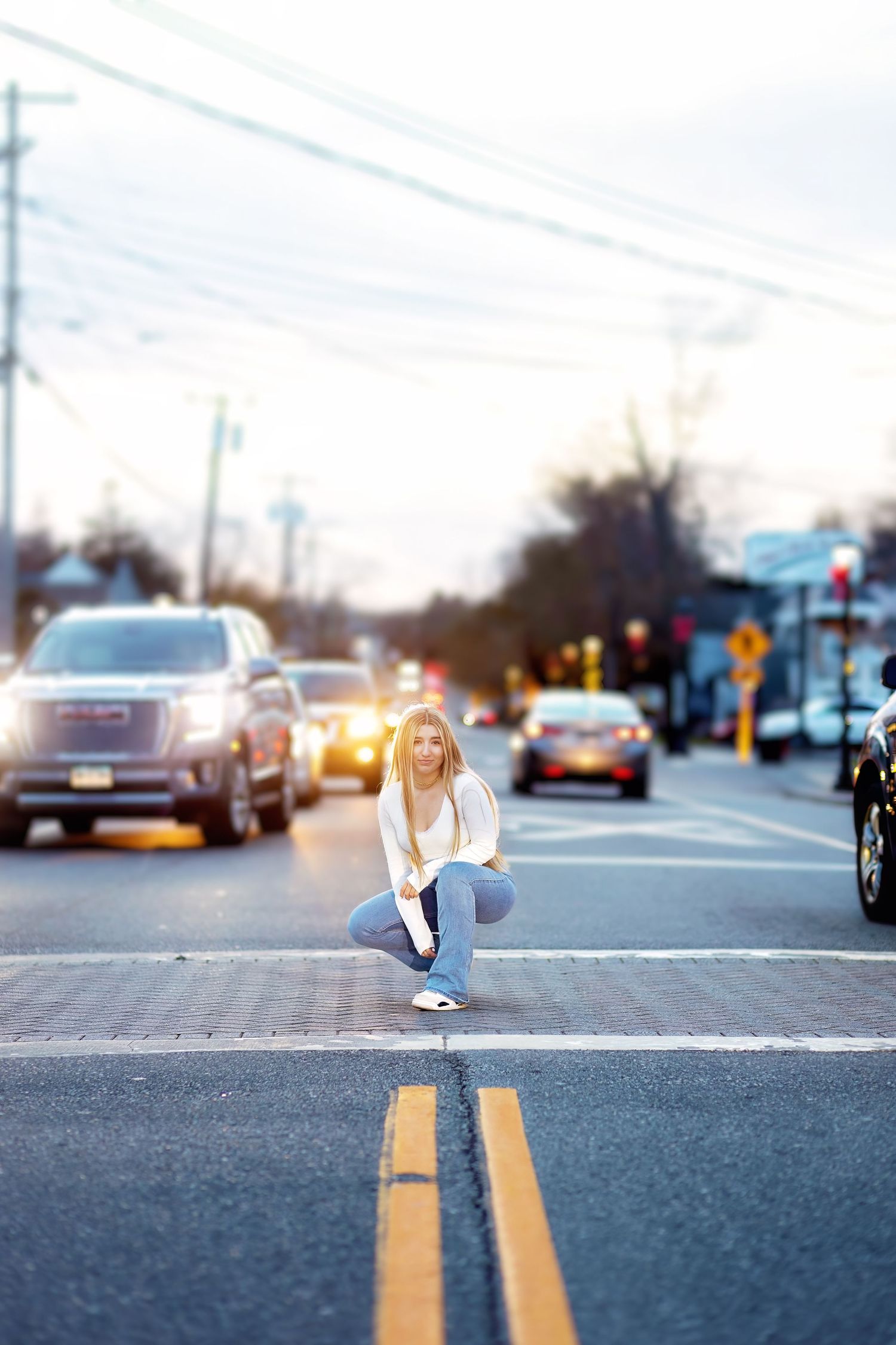 A person sits on double yellow road lines at dusk creating an artistic perspective shot on an empty street.
