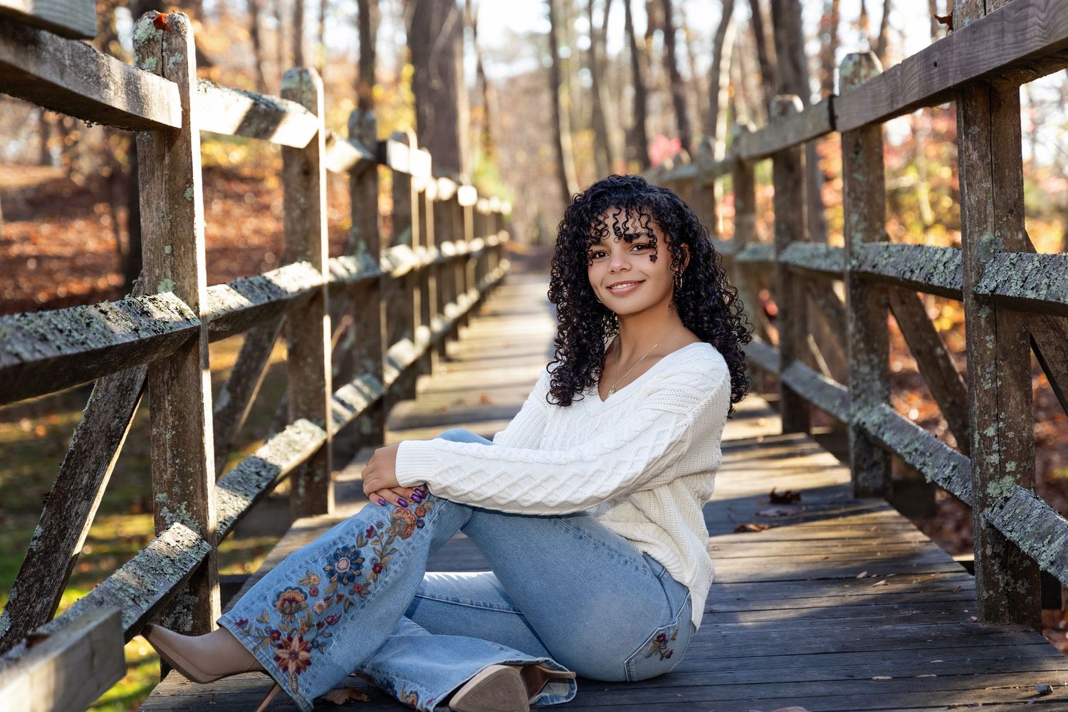 A person in casual attire poses on a wooden bridge surrounded by fall foliage.