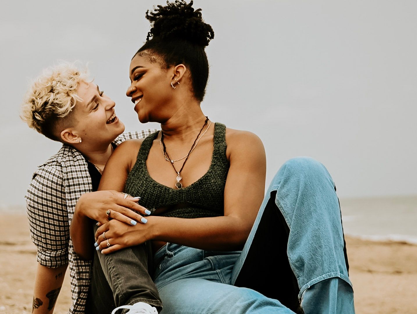 A couple shares joyful laughter while sitting together on a beach during sunset.