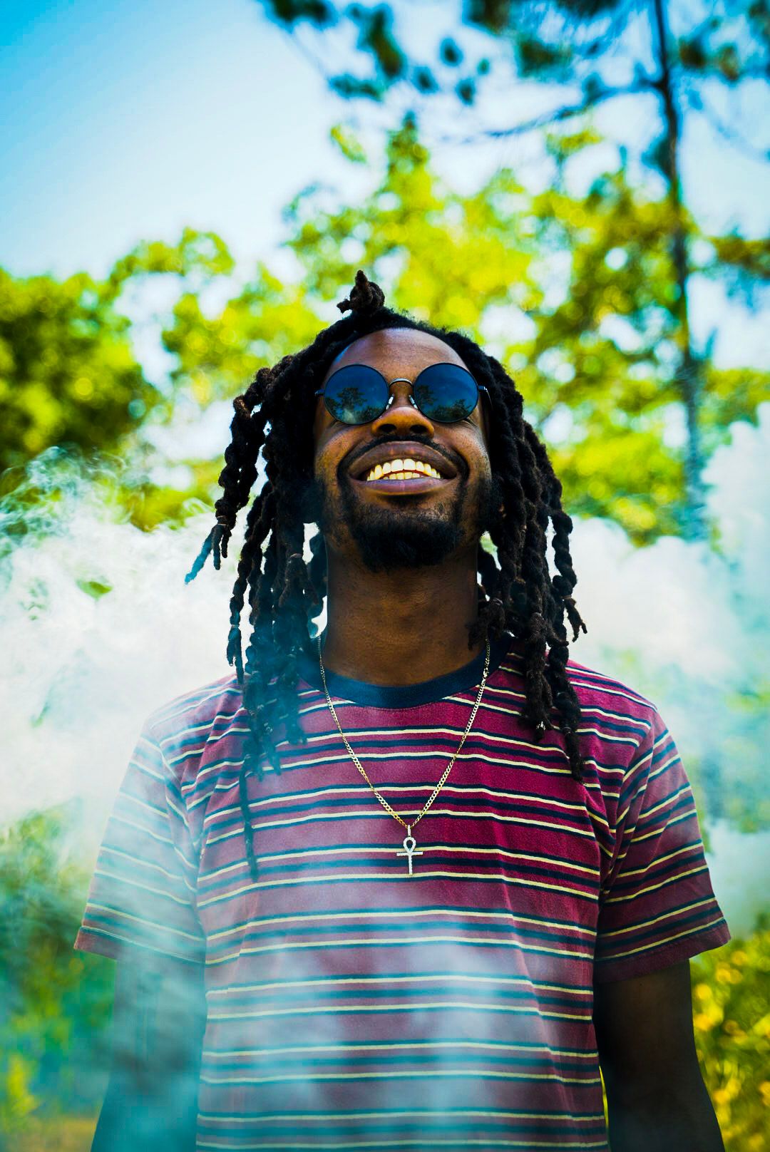 Person wearing sunglasses and striped shirt laughing against bright blue sky and trees.