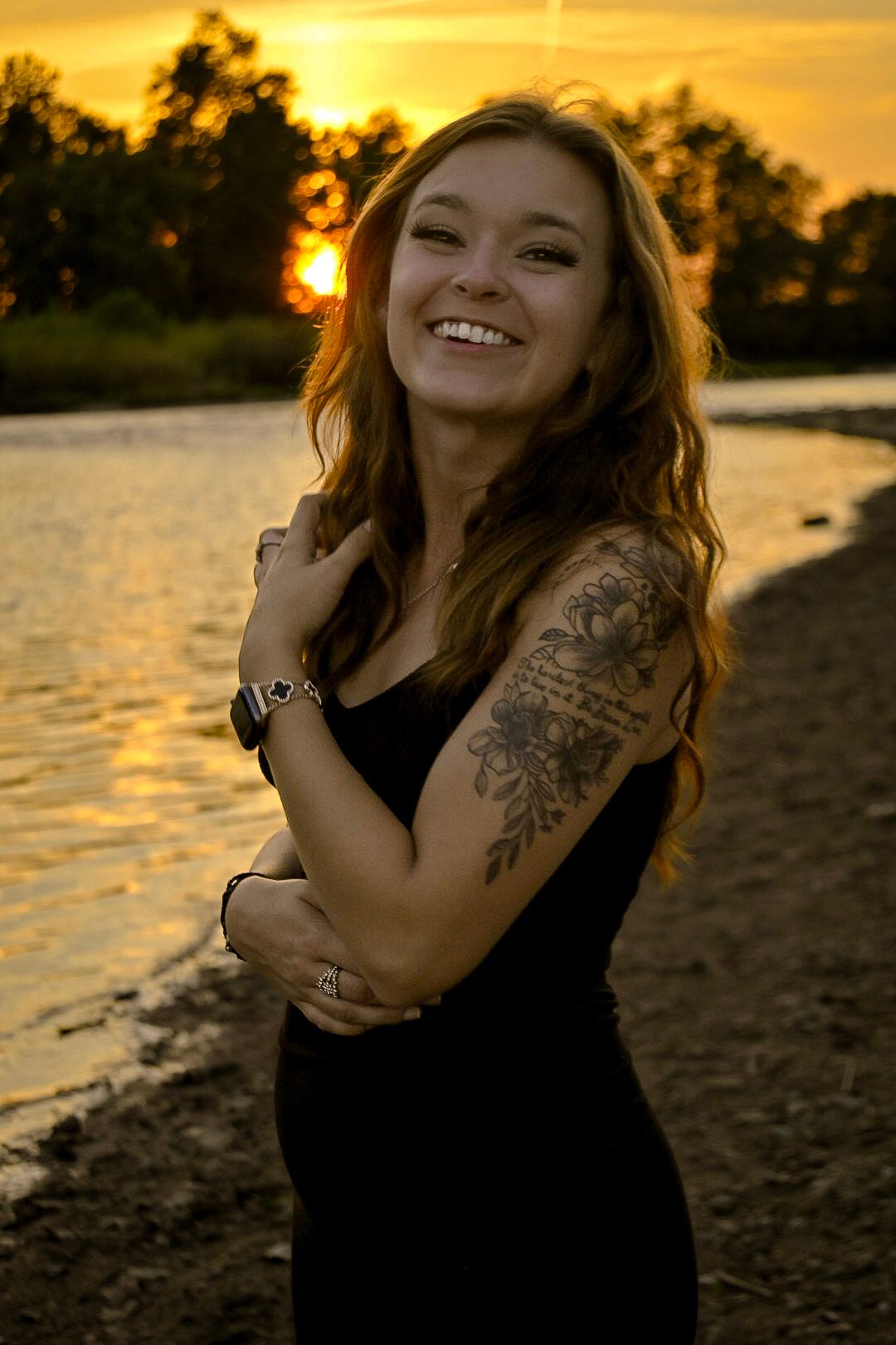 Portrait at golden hour sunset by water with visible tattoo and natural smile.