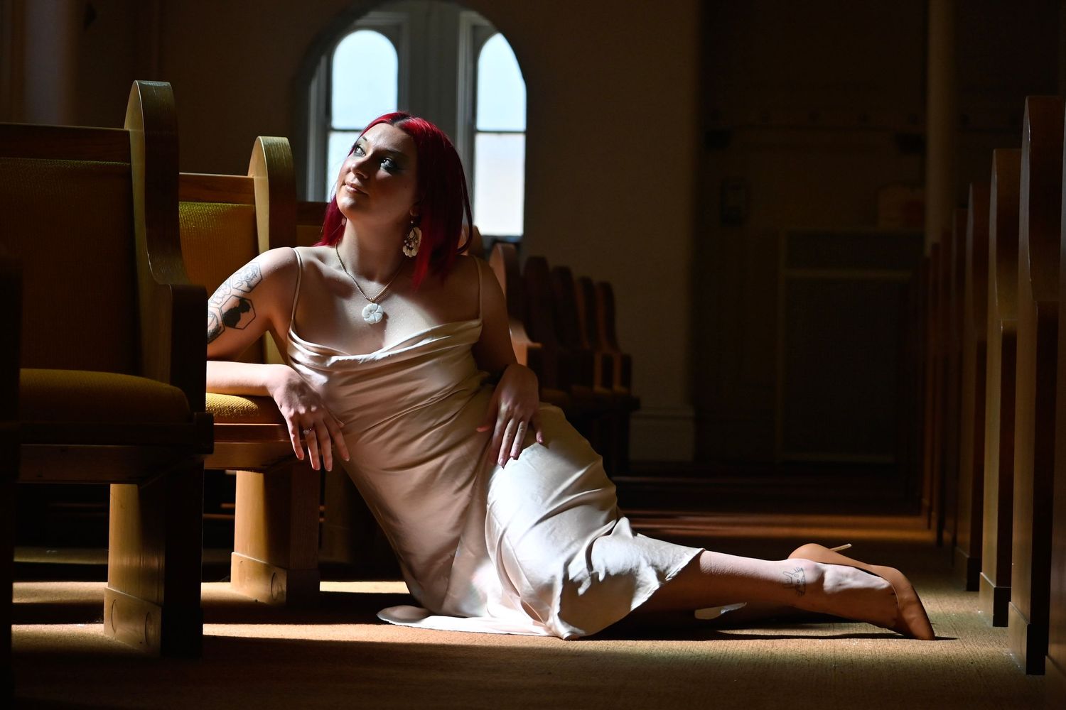 A dancer in a white dress poses dramatically in a sunlit church interior with arched windows.