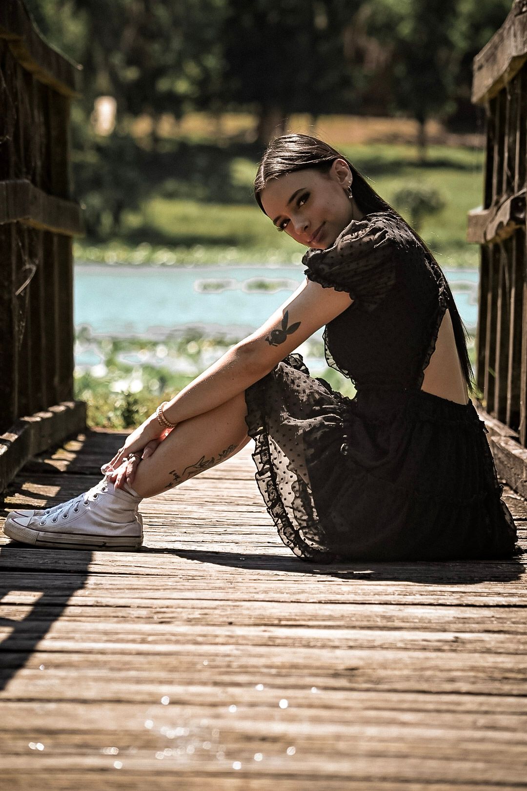 Person resting on wooden dock by lake in black dress during afternoon light.