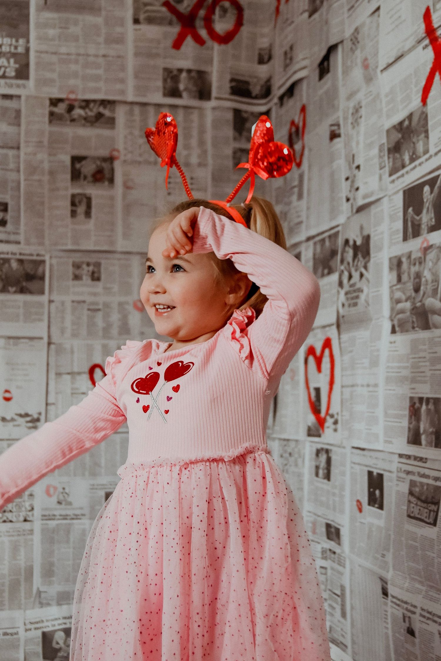 A pink tulle dress with red hearts decorates a room with newspaper-covered walls.