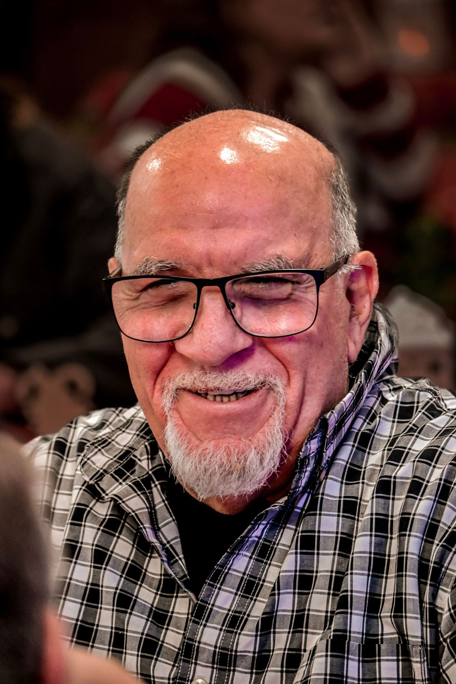 A cheerful older man in glasses and plaid shirt laughing heartily.