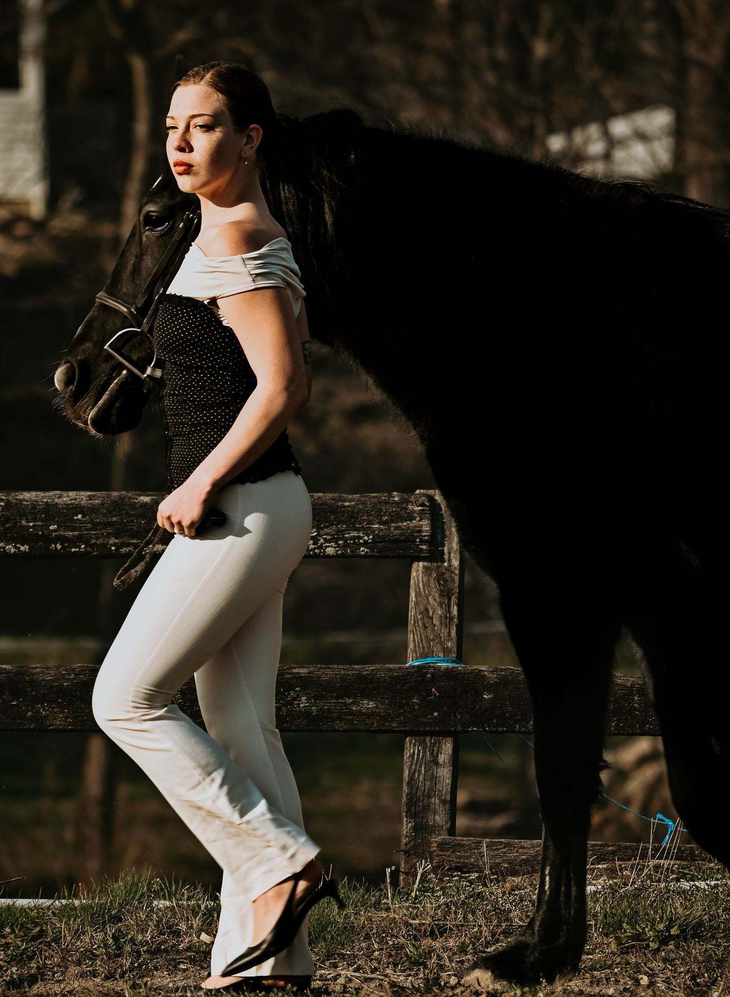 A bride in a sleek white dress poses elegantly against rustic wooden fencing at sunset.