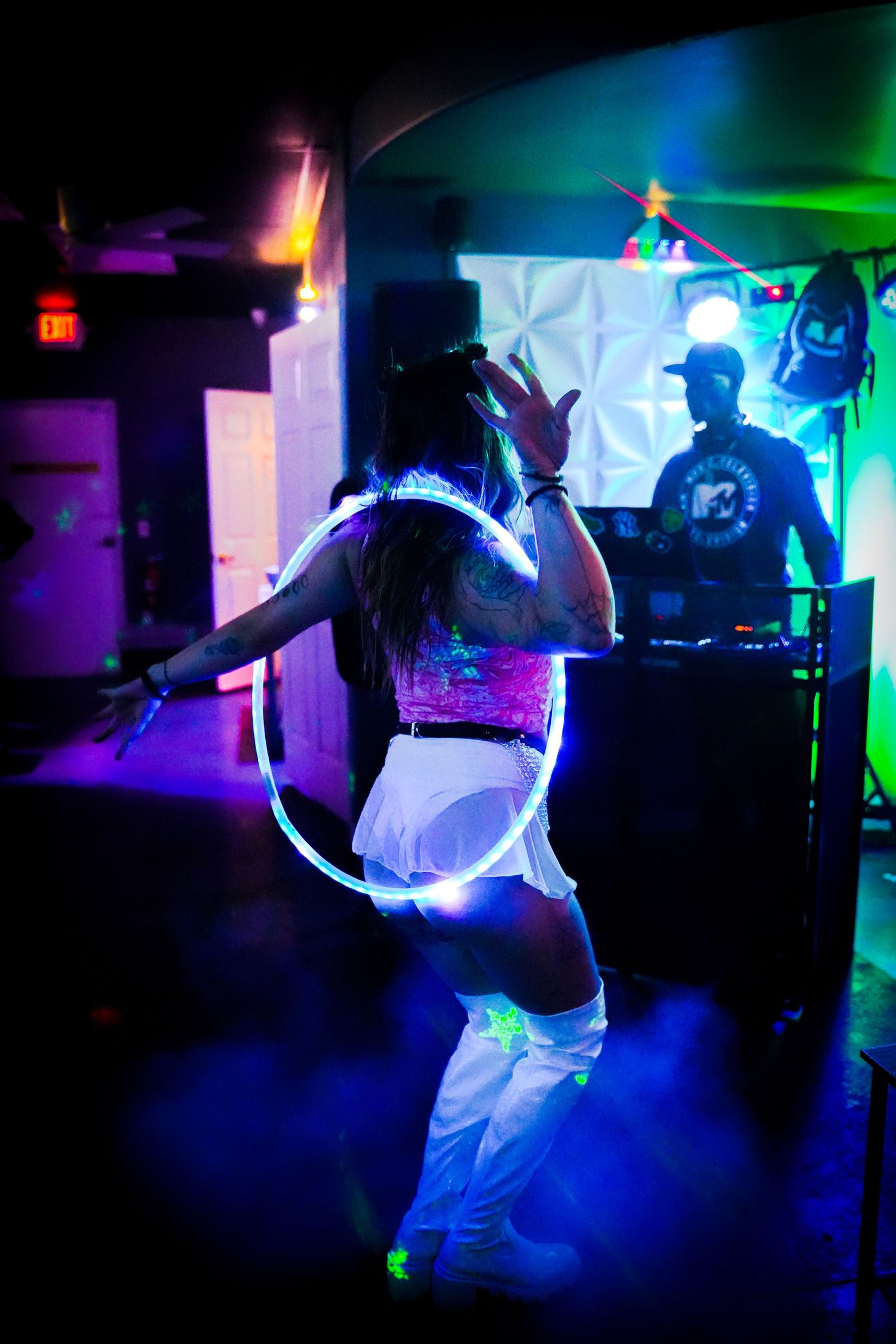 Dancers in white outfits performing under colorful neon lights in a dark venue.