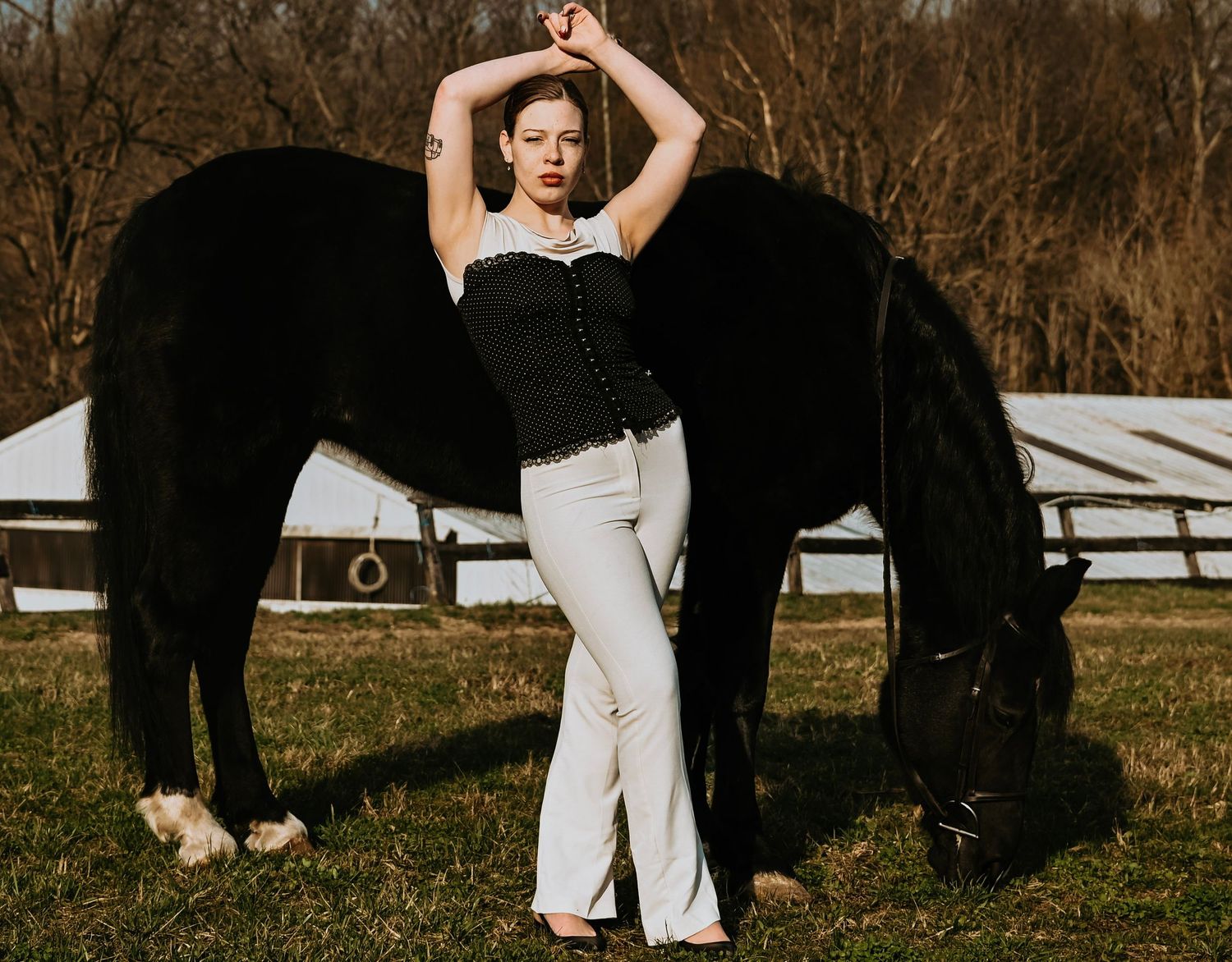 Elegant couple dances gracefully in front of a black horse on a rustic farm with white fencing in autumn.