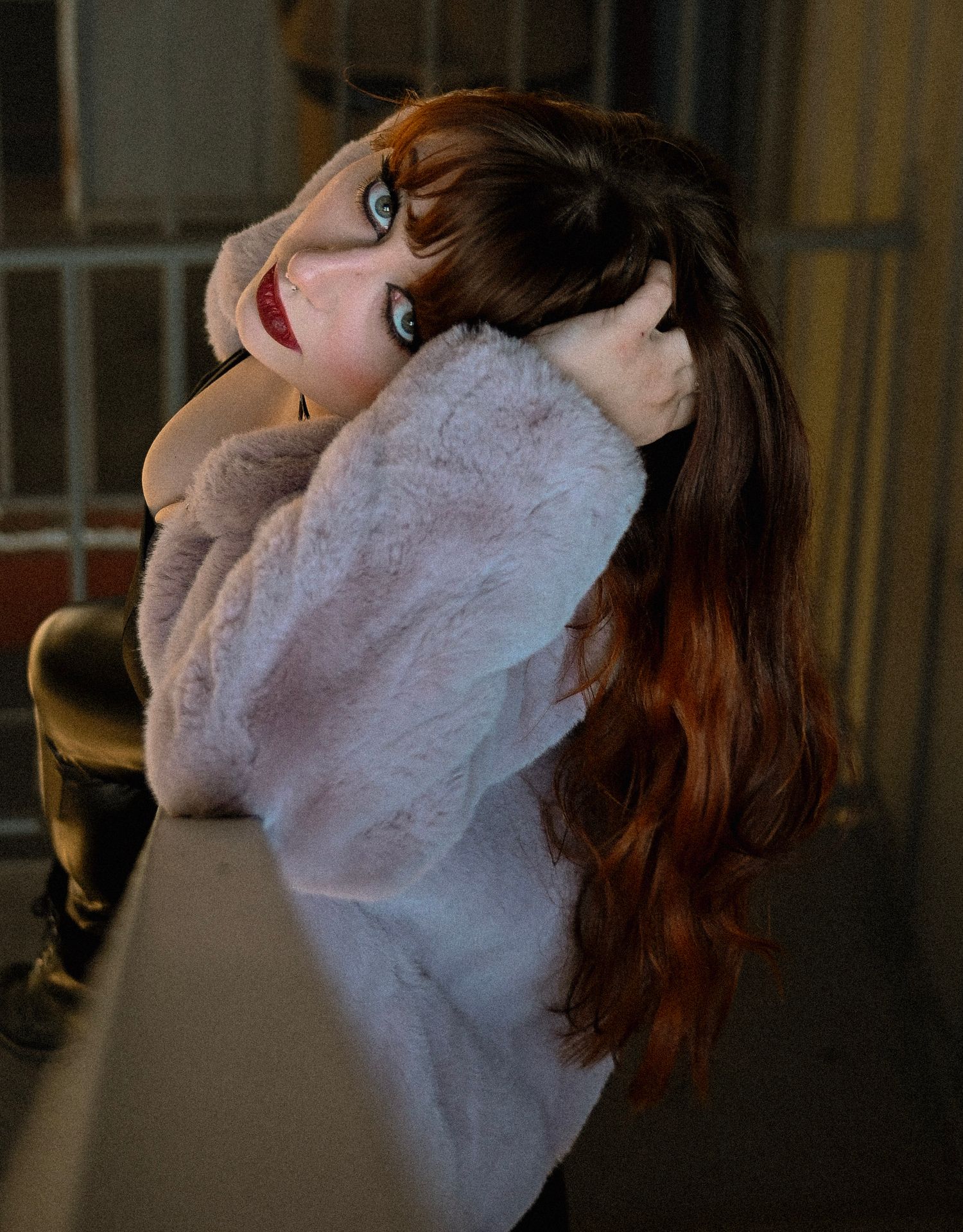 A young woman with long red hair poses in a white faux fur coat, glancing over her shoulder outdoors at night.