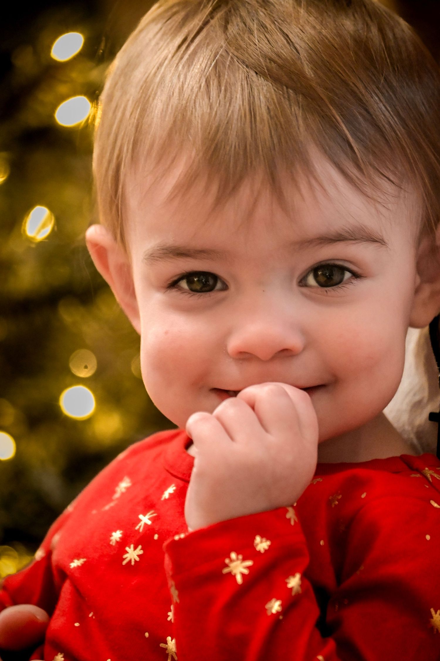 Young child in red star-patterned clothing covering their mouth while smiling.