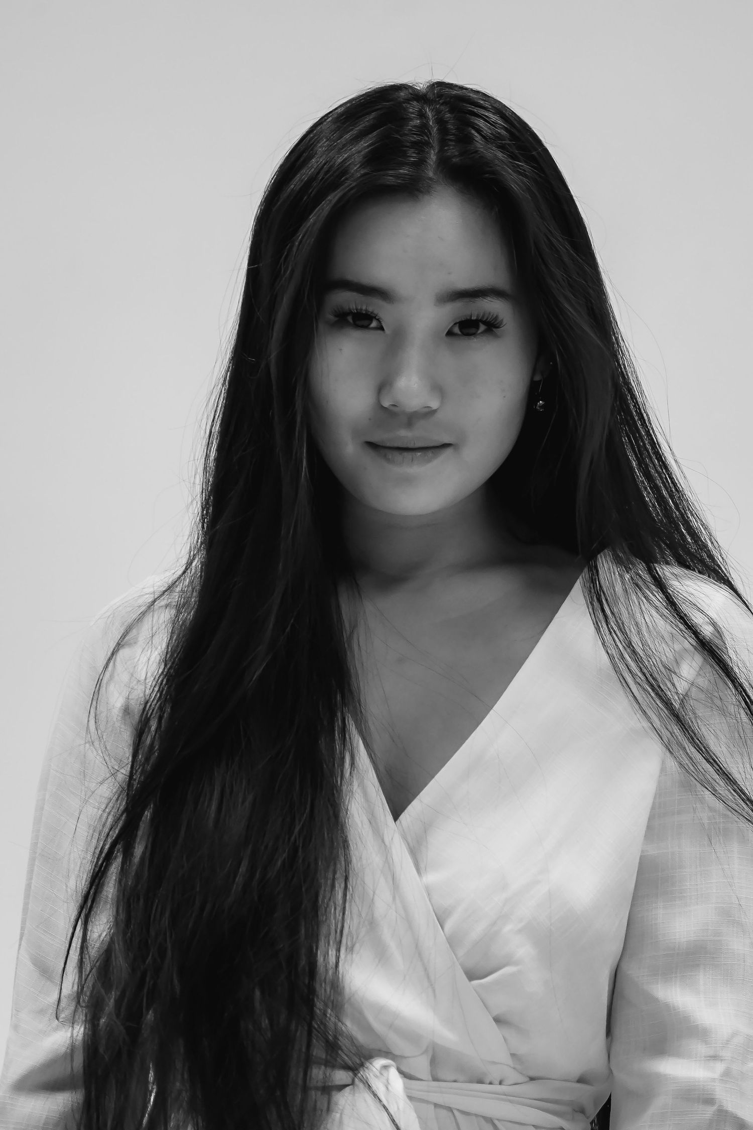 Black and white portrait of woman in white wrap dress with long dark hair against light background.