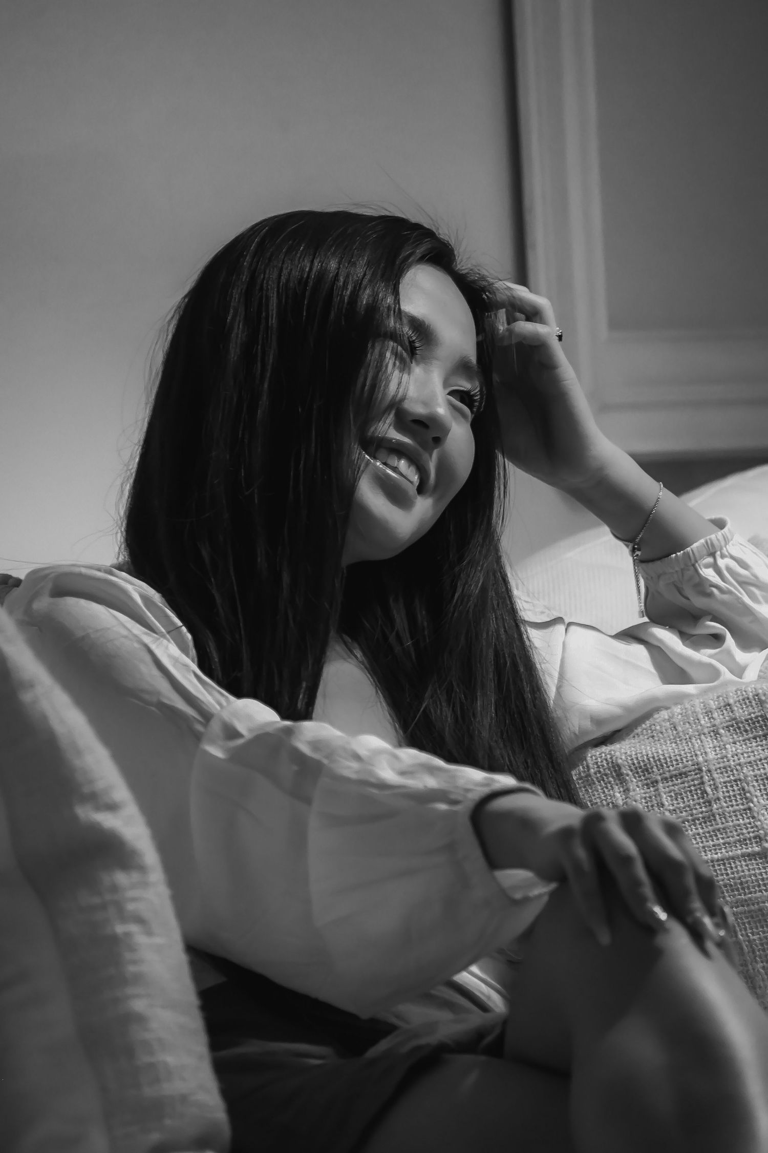 Black and white photo of woman in white top relaxing on couch with natural window light.