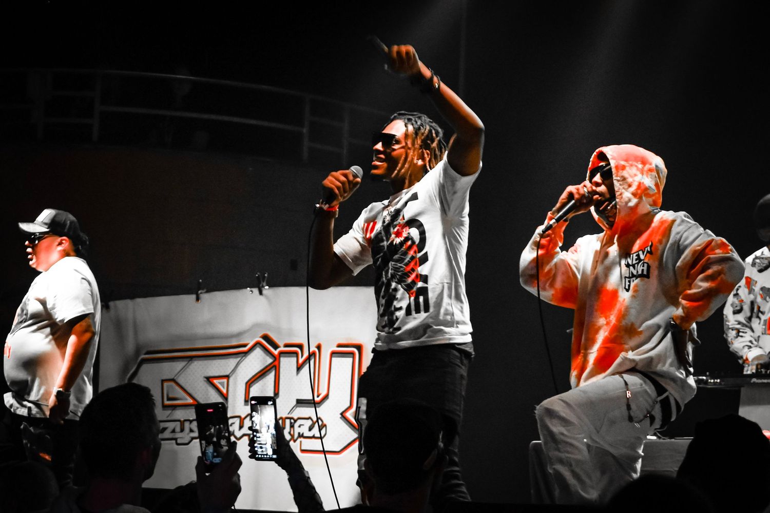 Performers on stage in orange and white outfits during a dynamic concert performance.