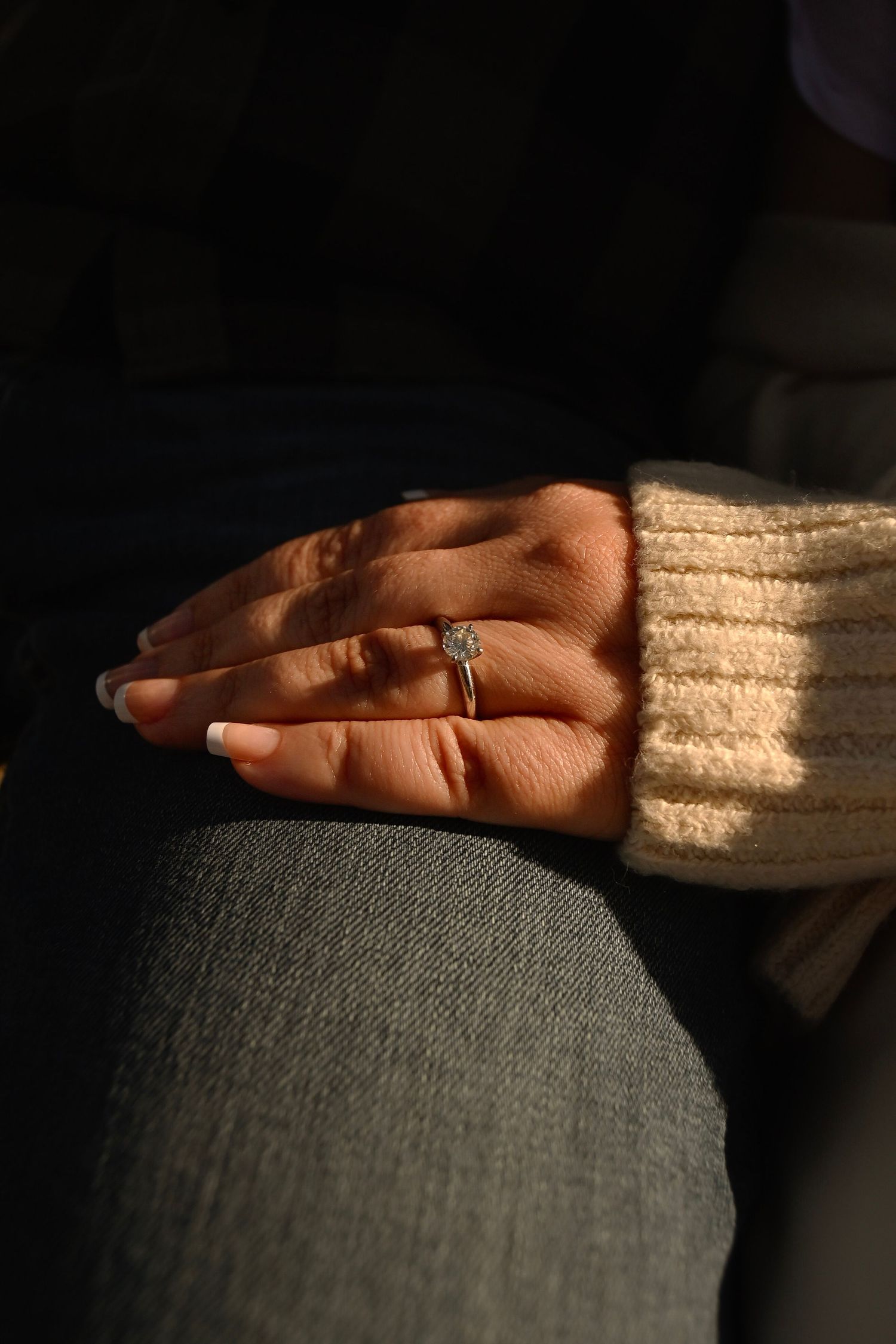 A hand rests gently on a textured gray fabric surface next to cream-colored material in dim lighting.