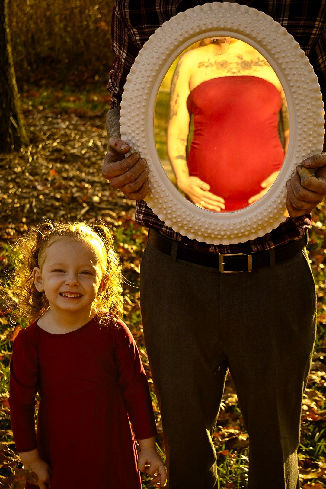 A pregnancy announcement photo using a decorative white frame in autumn sunlight.