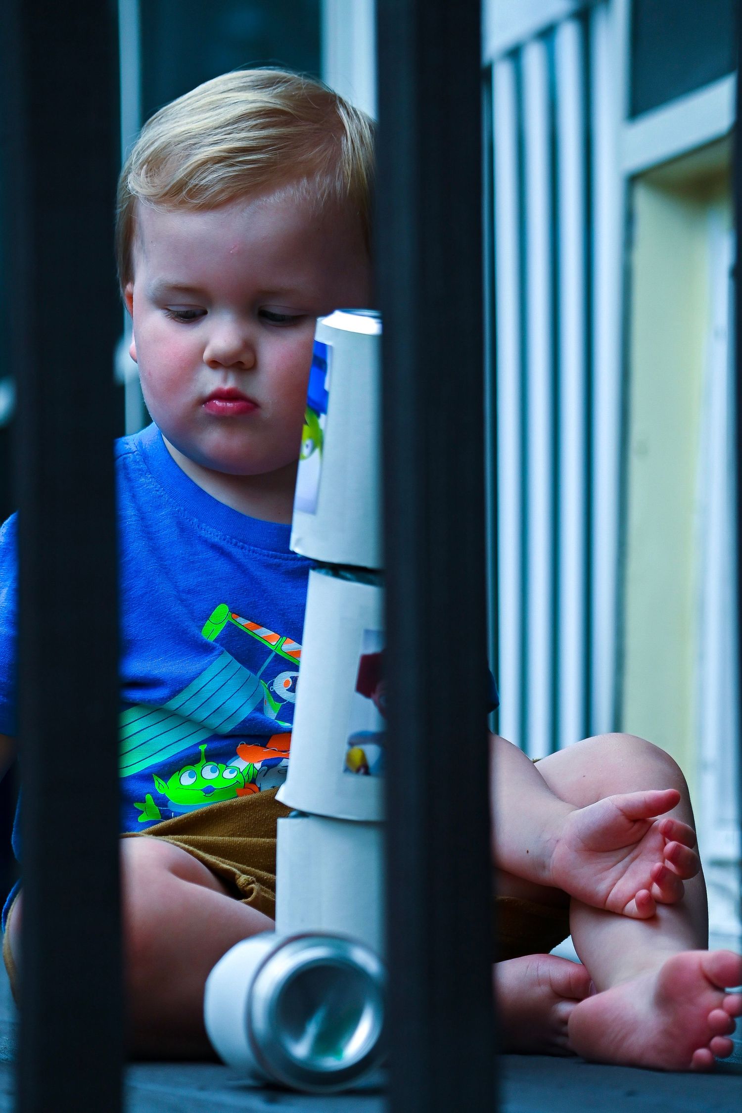 Young child in blue clothing examining something through white bars.